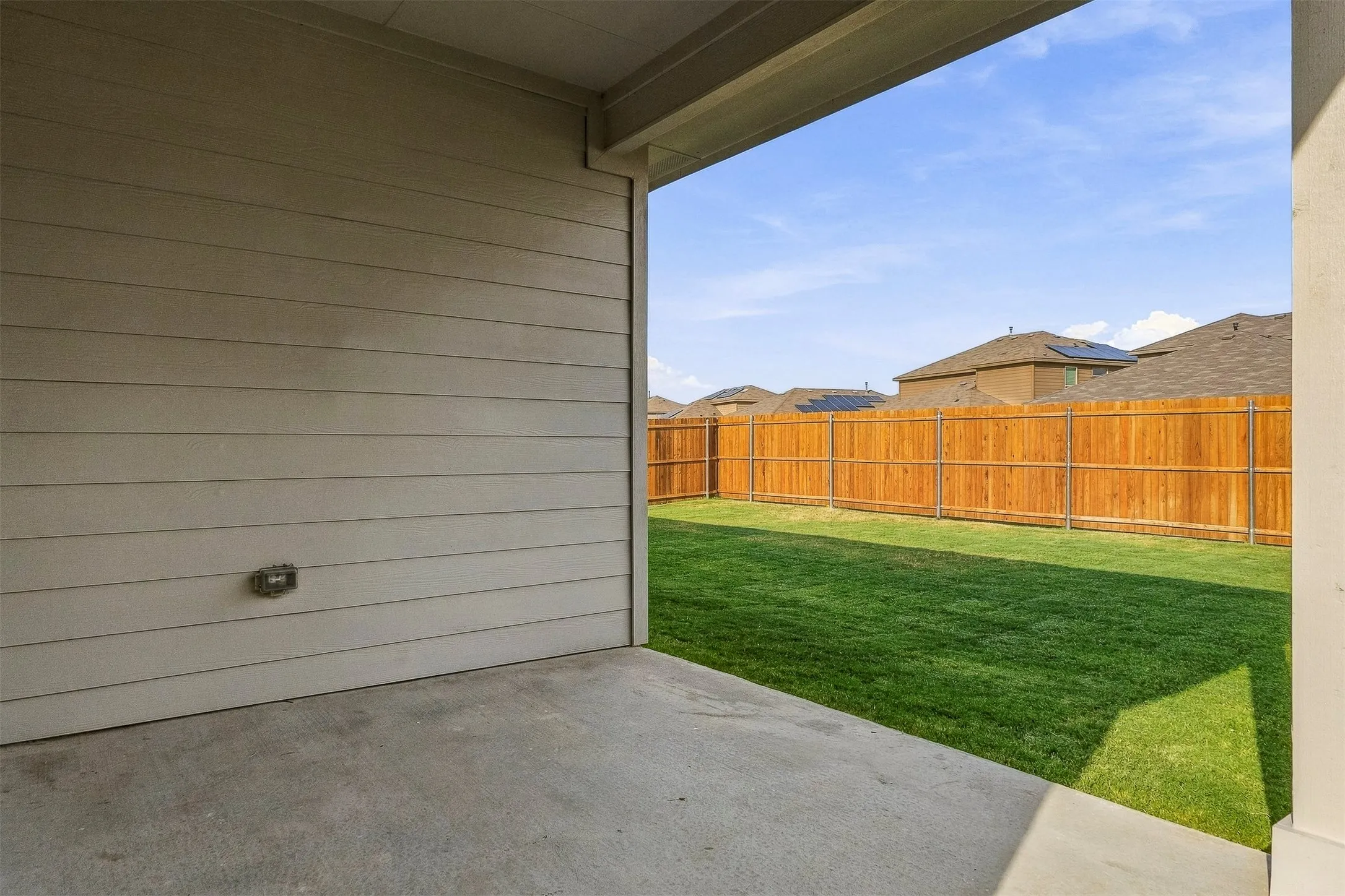 Covered concrete patio with siding exterior, opening to a fenced backyard featuring a manicured lawn