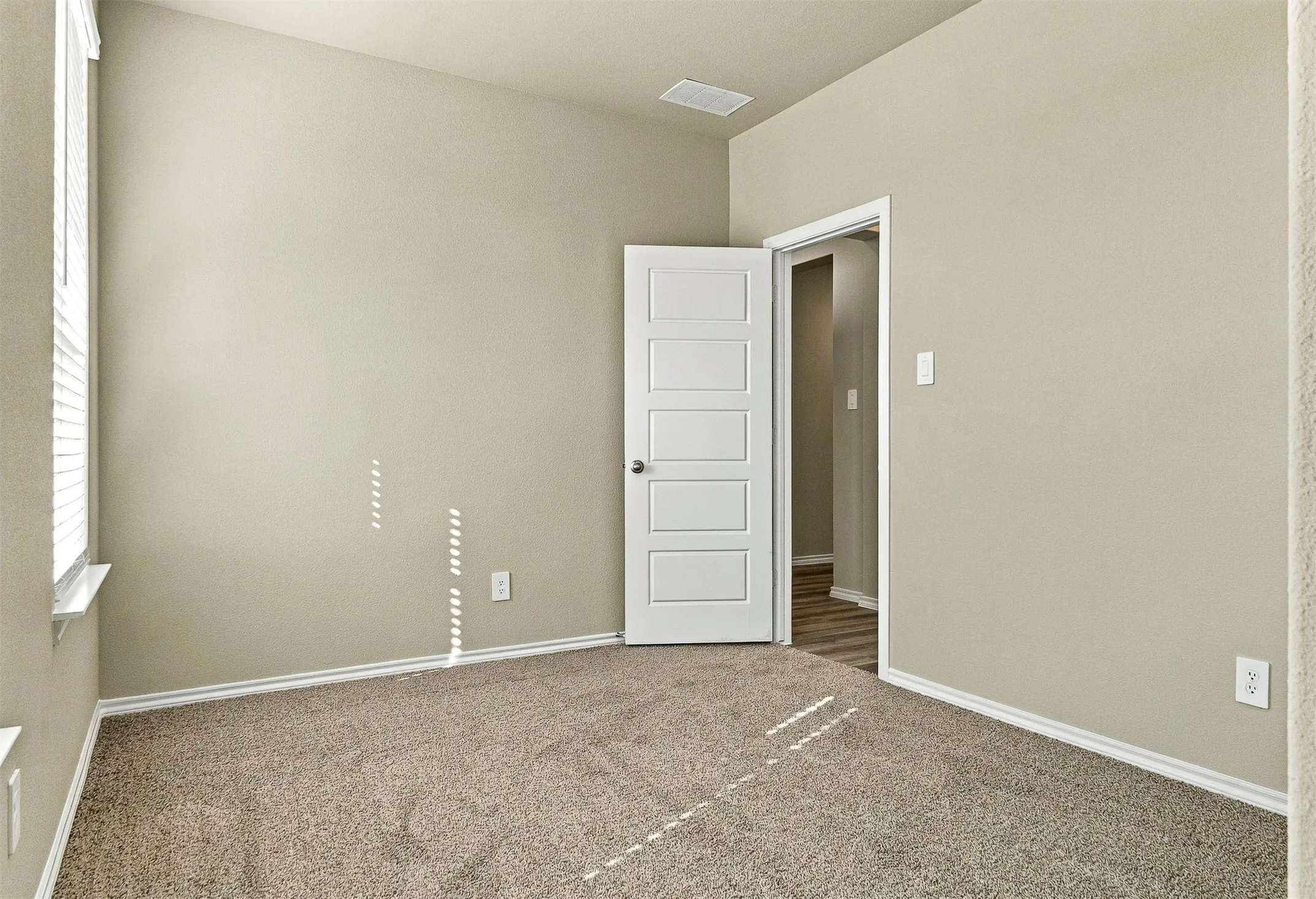 Neutral wall finish, carpeted flooring, white trim details, window with blinds, and a five-panel interior door