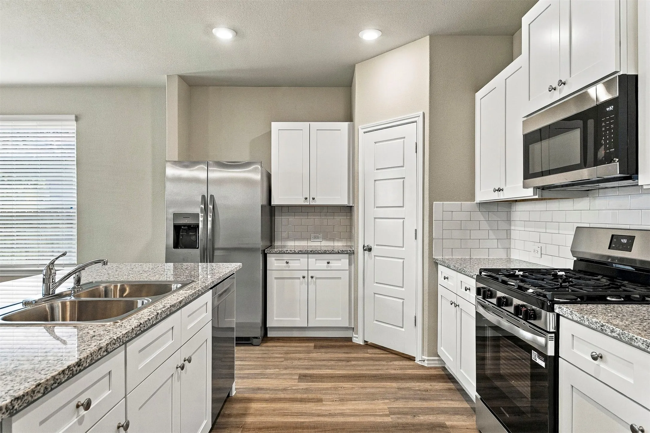 Kitchen featuring white cabinetry, wood-finish flooring, stainless steel appliances, a dual basin sink, and subway tile backsplash