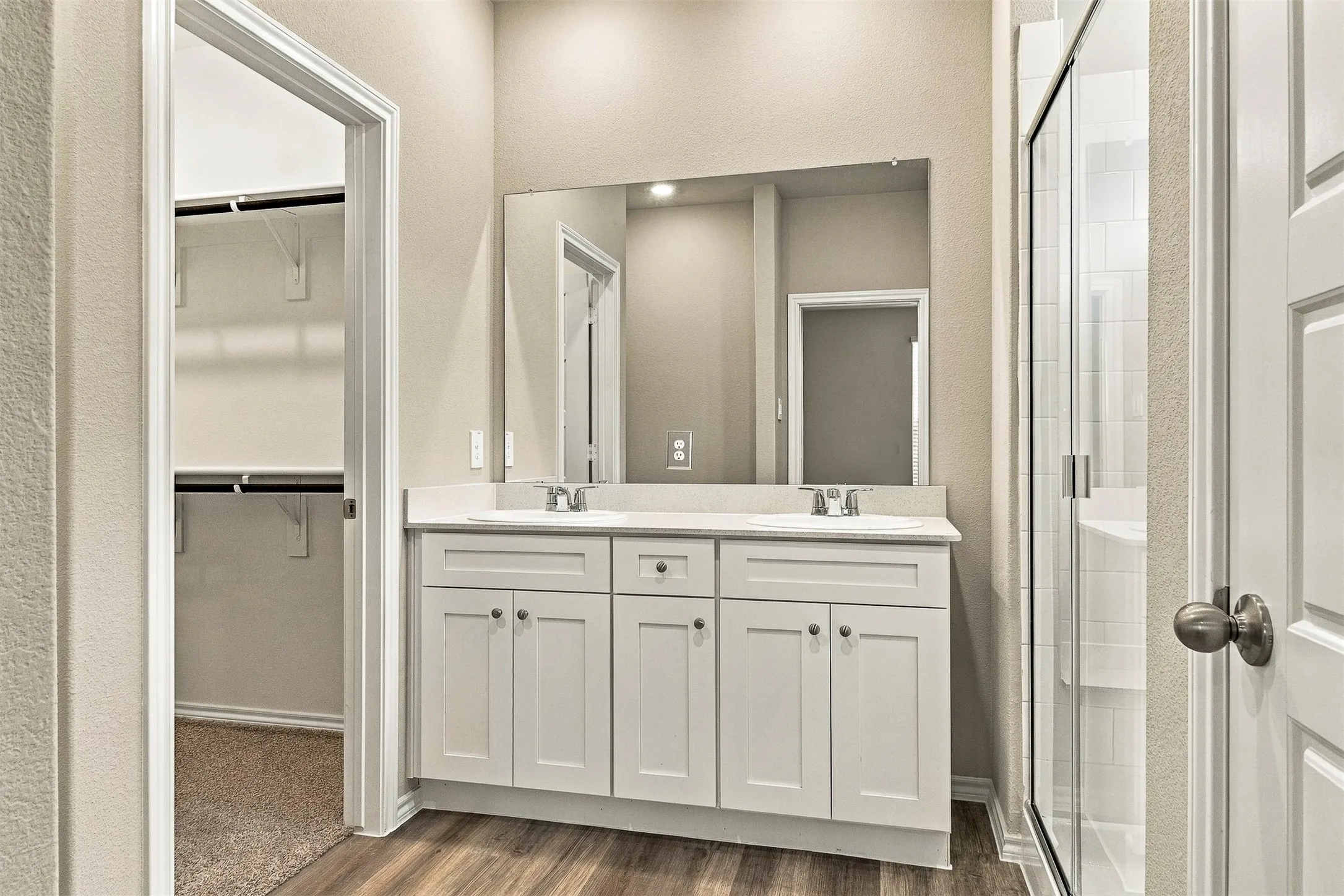 Dual vanity with integrated sinks, wood-finish flooring, frameless glass shower enclosure, and built-in closet shelving