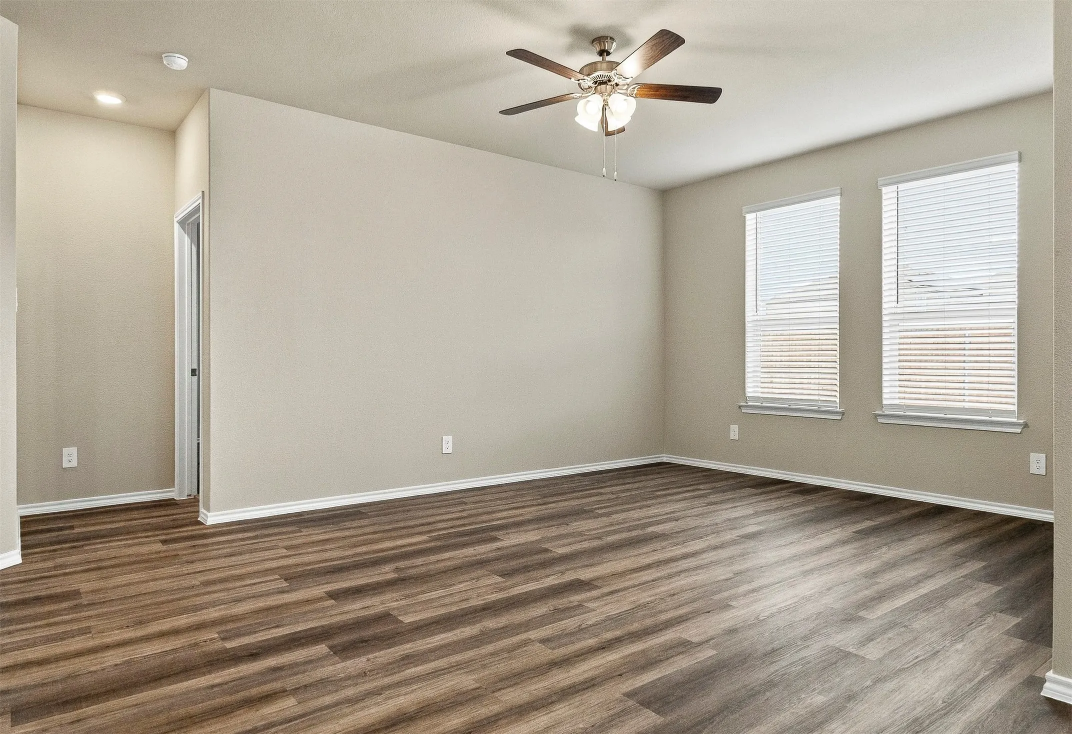 Spacious room featuring wood-finish flooring, neutral-toned walls, and a ceiling fan