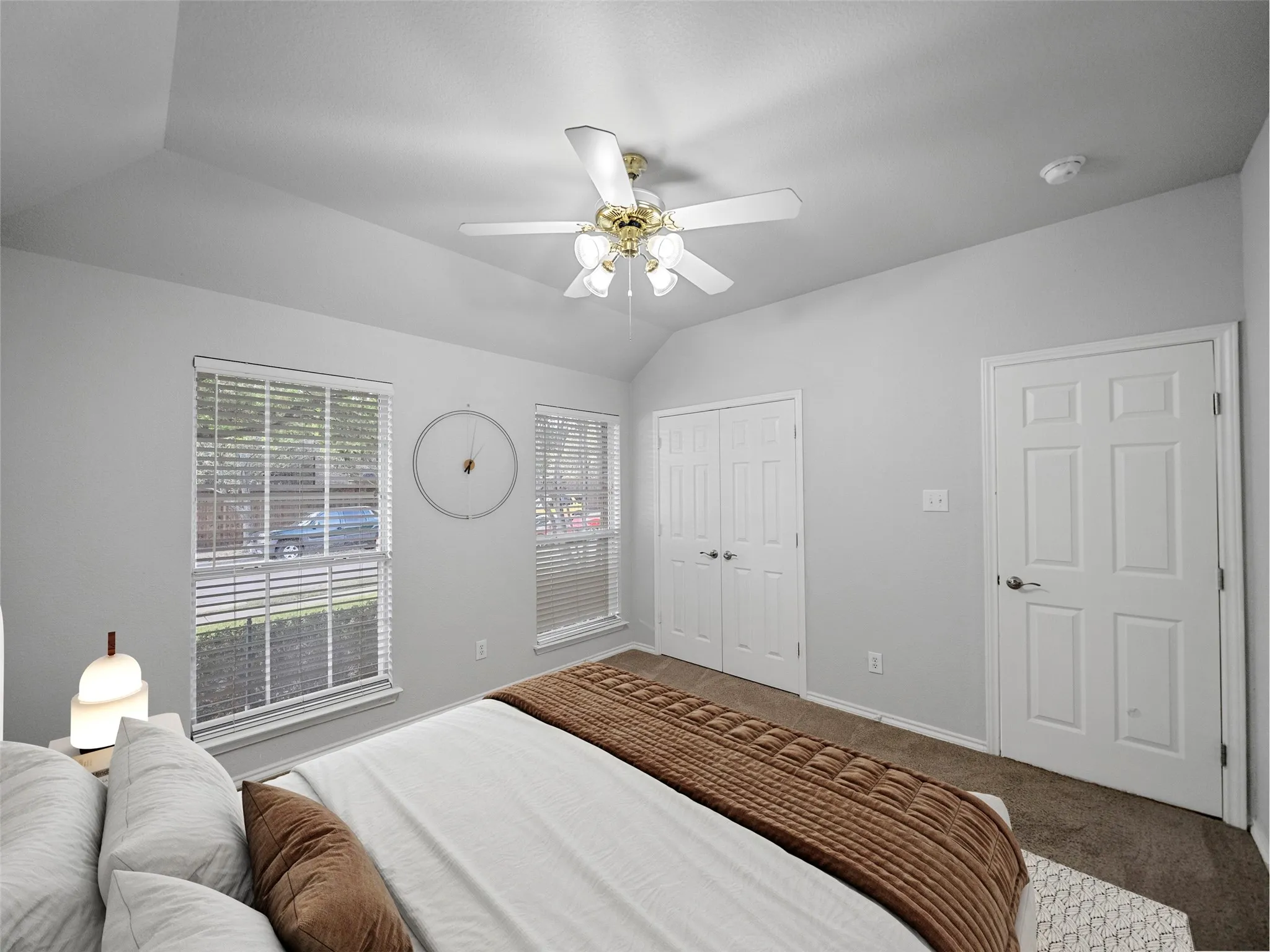 Vaulted ceiling with an attached ceiling fan, dual windows with blinds, and white paneled doors