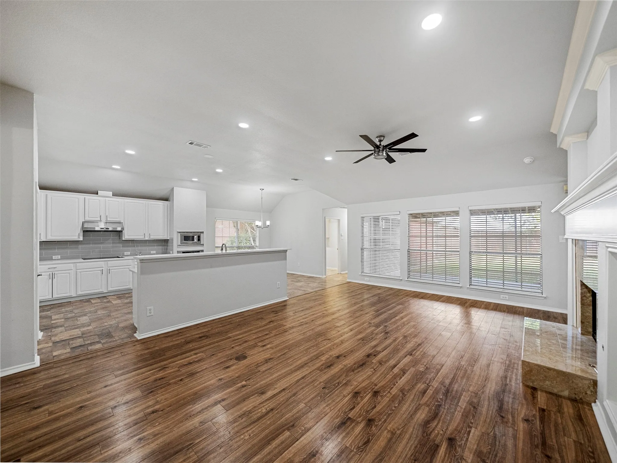 Vaulted ceiling, recessed lighting, wood-finish flooring, white kitchen cabinetry, and a fireplace with a stone hearth
