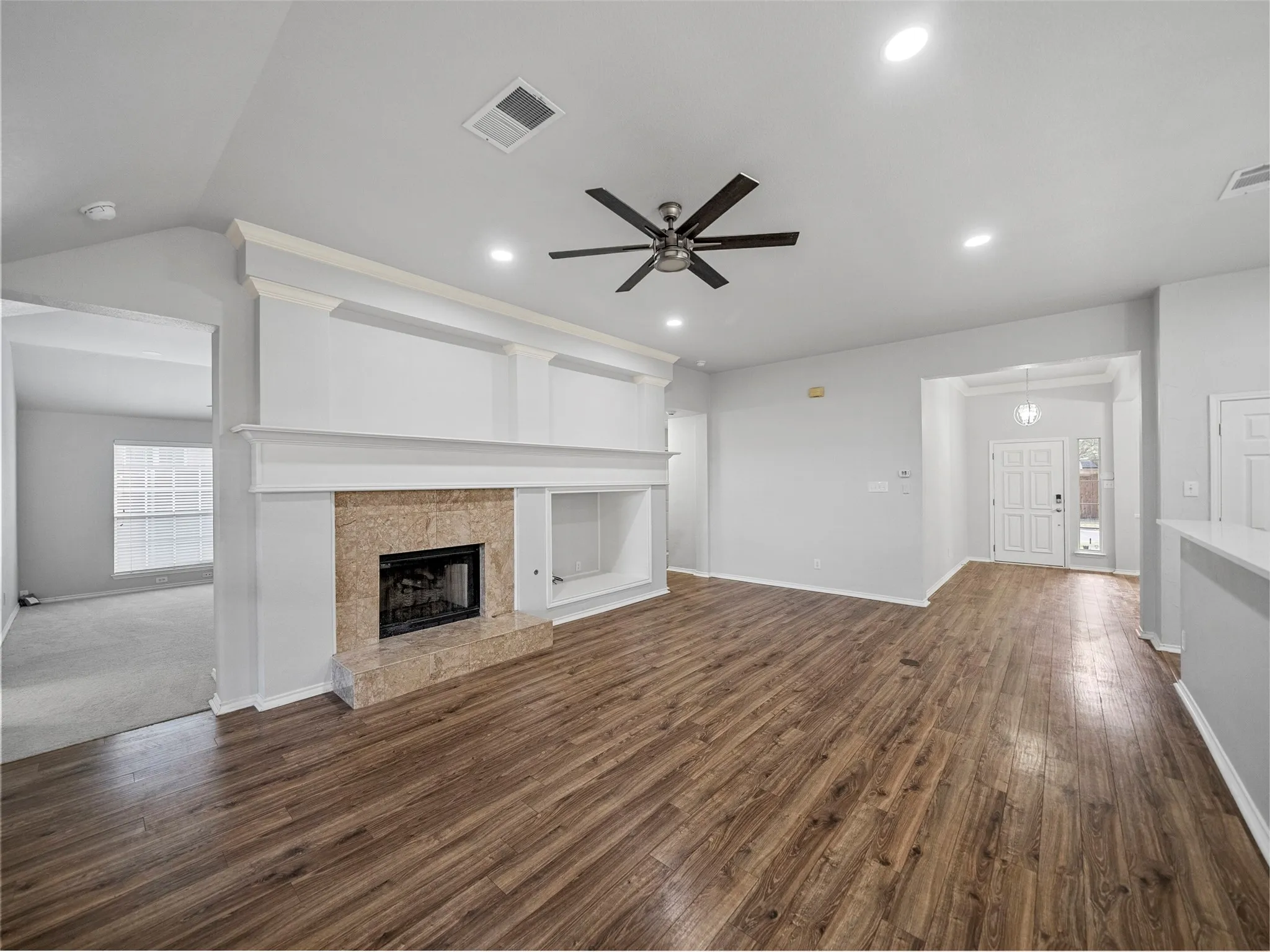 Spacious living area featuring wood-finish flooring, a built-in fireplace with a stone surround, and overhead recessed lighting
