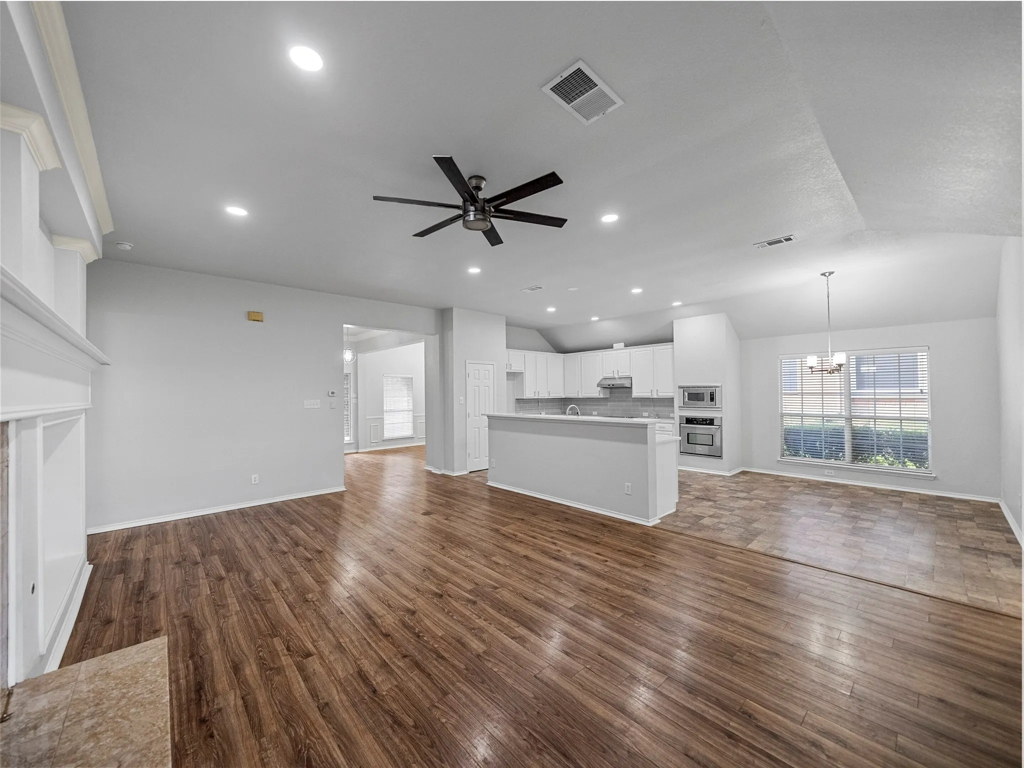 Open-concept living area with wood-finish flooring, a contemporary ceiling fan, recessed lighting, and a kitchen featuring white cabinetry, a built-in microwave, and an oven