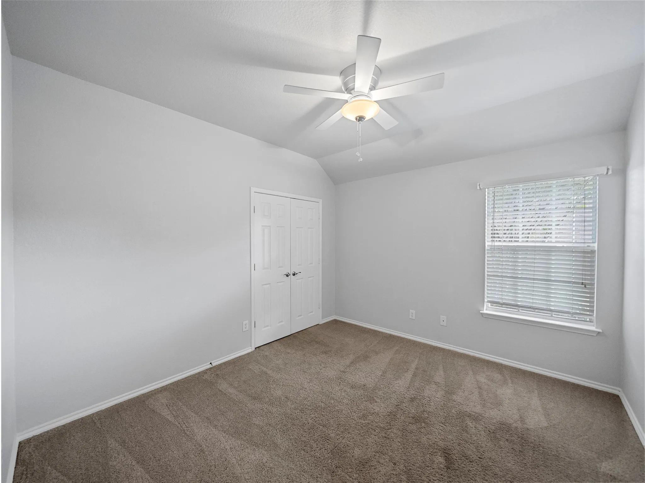 Sloped ceiling featuring a ceiling fan with integrated lighting, carpeted flooring, window with blinds, and white bi-fold doors