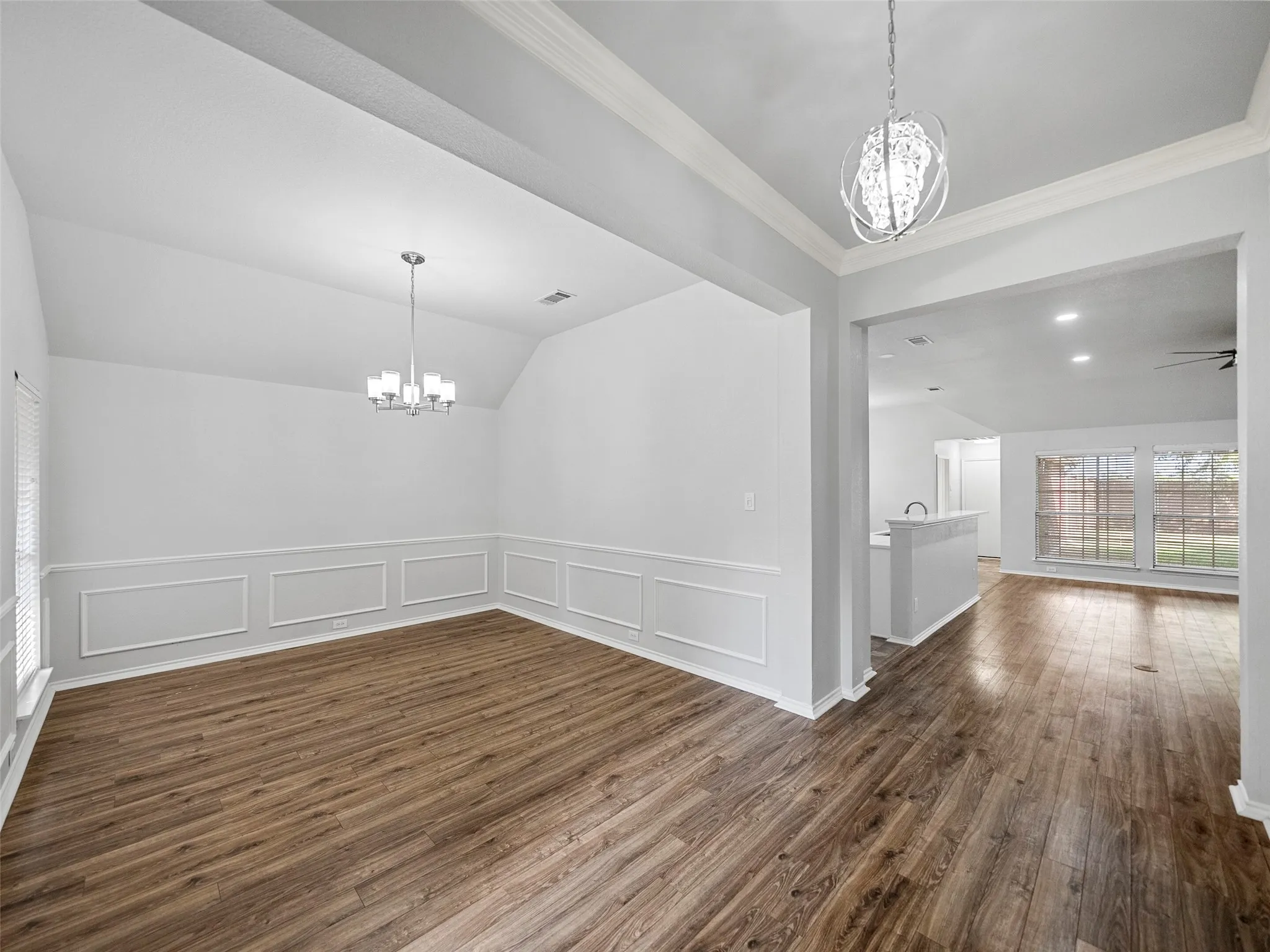 Wood-finish flooring throughout, vaulted ceiling, decorative wall molding, and contemporary chandeliers