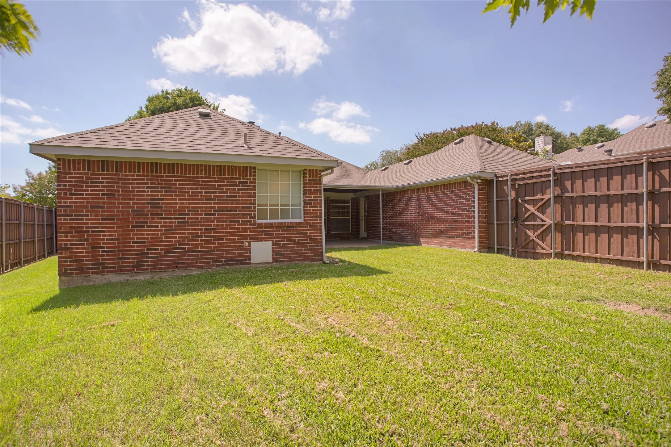 Expansive backyard with a manicured lawn, brick exterior, fenced perimeter, and a covered patio area