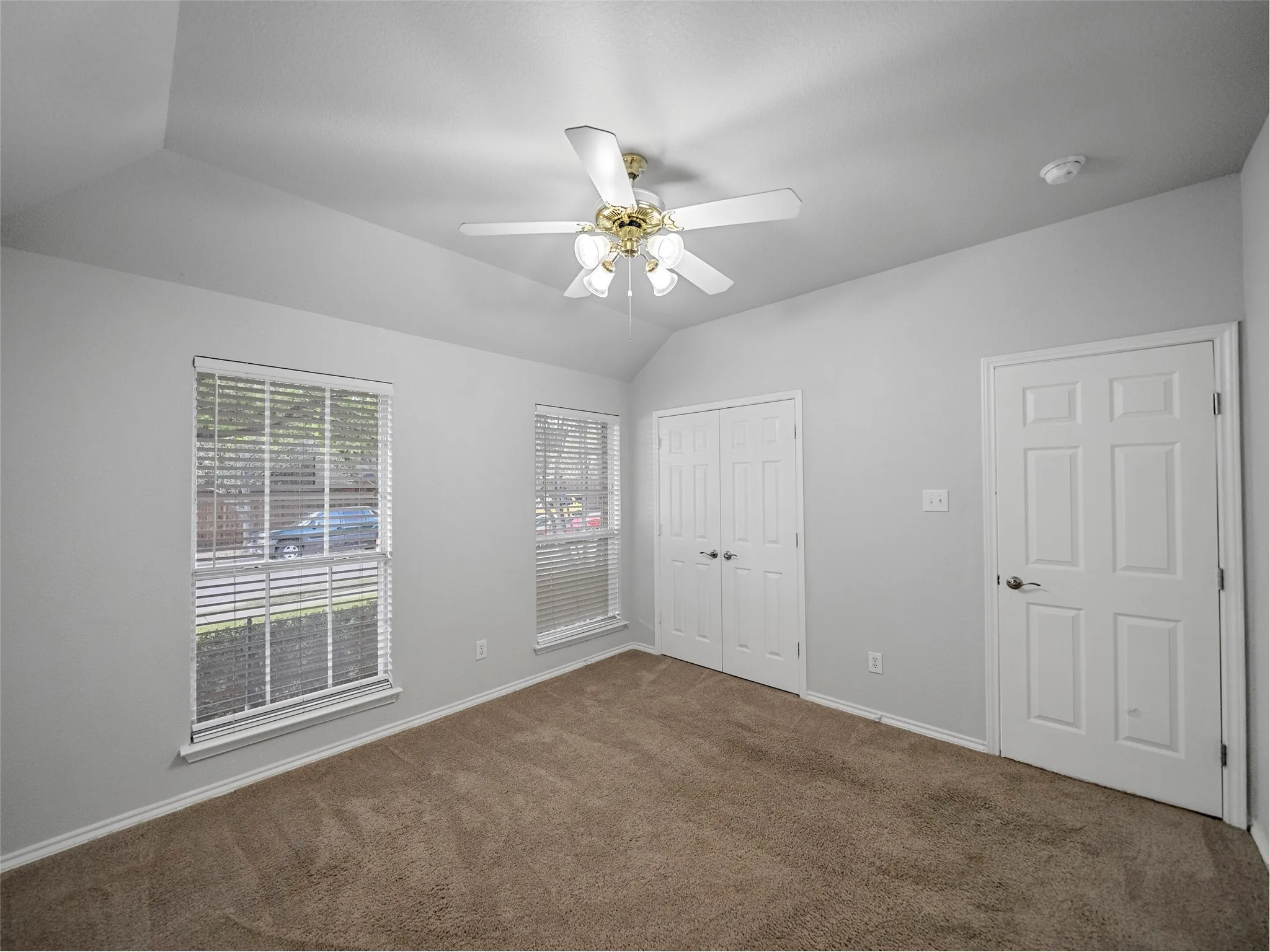 Vaulted ceiling, two windows with blinds, carpet flooring, bi-fold closet doors, and a ceiling fan with light fixture