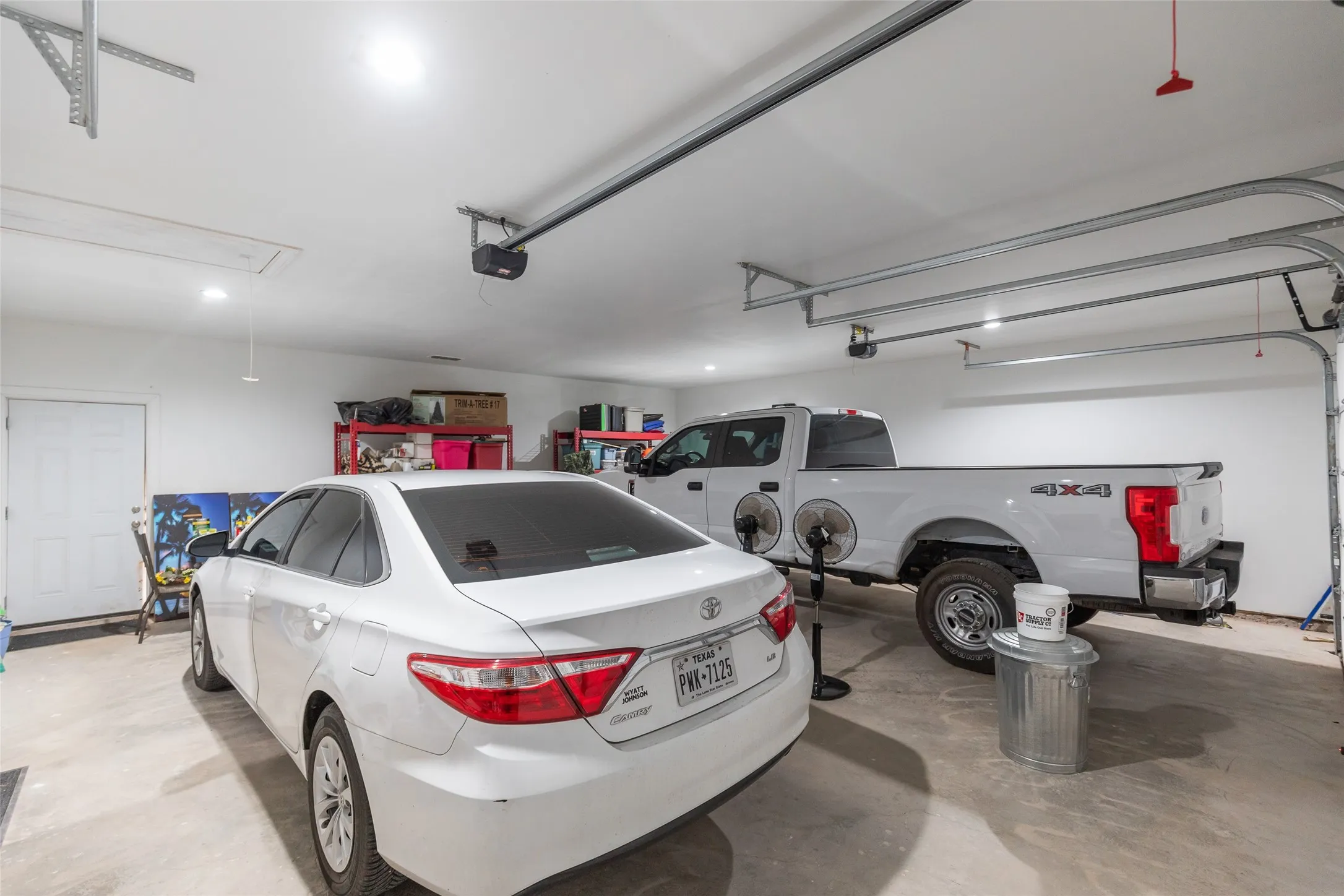 Attached two-car garage featuring a concrete floor, bright overhead lighting, and two automatic garage door openers