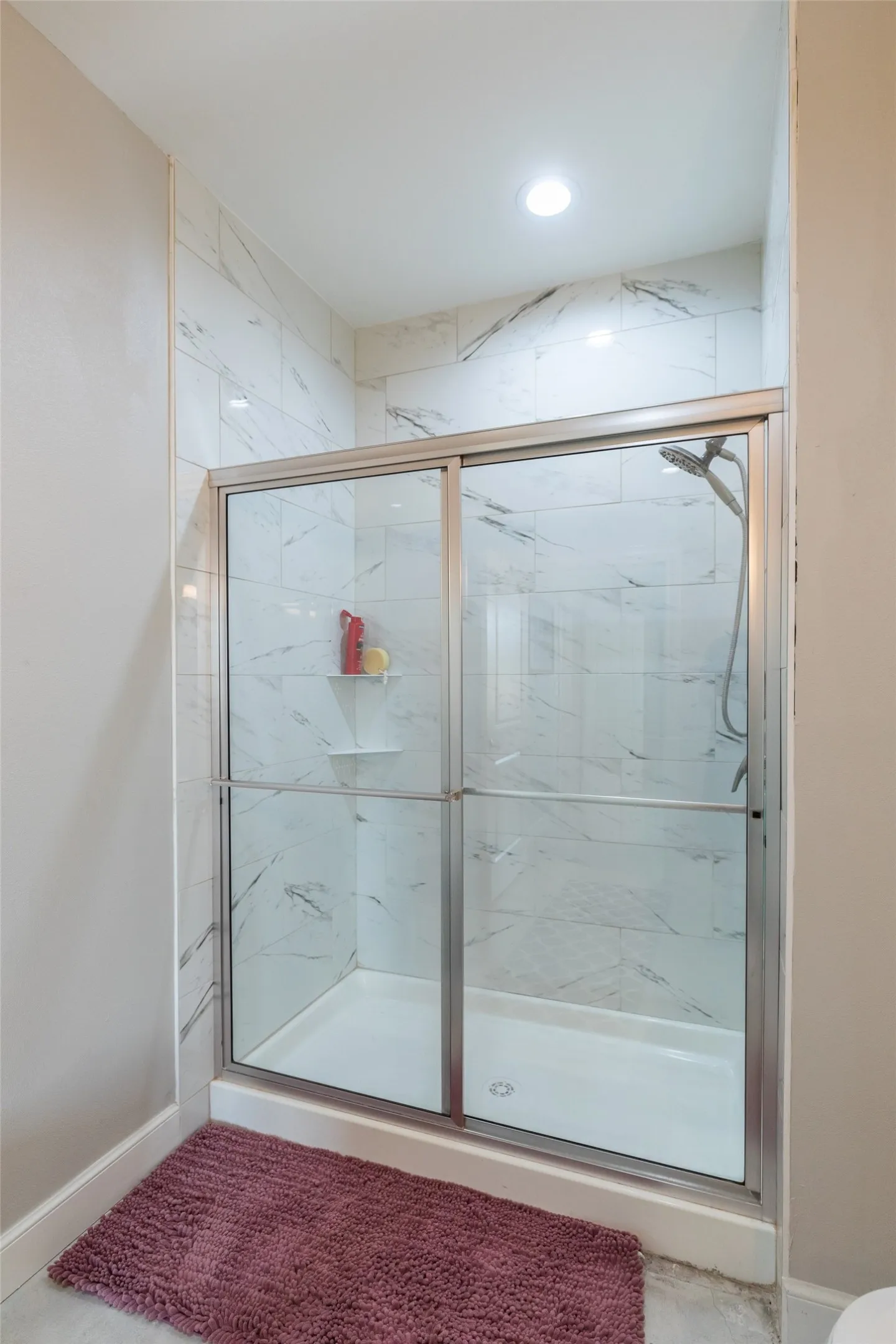 Enclosed shower with sliding glass doors, white tiled walls with subtle veining, recessed lighting, and a built-in shower niche