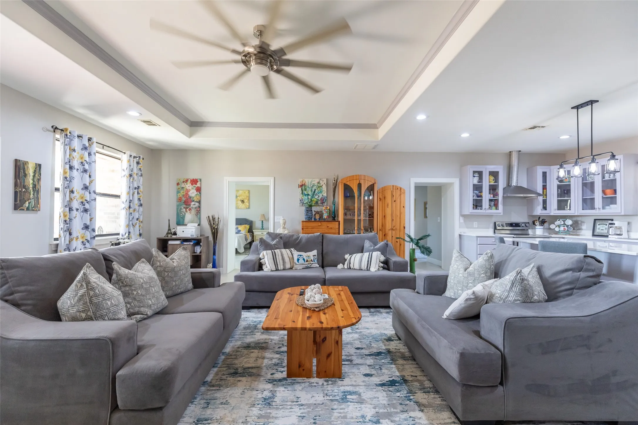 Tray ceilings with recessed lighting, kitchen with white cabinetry, stainless steel range hood, and pendant lighting