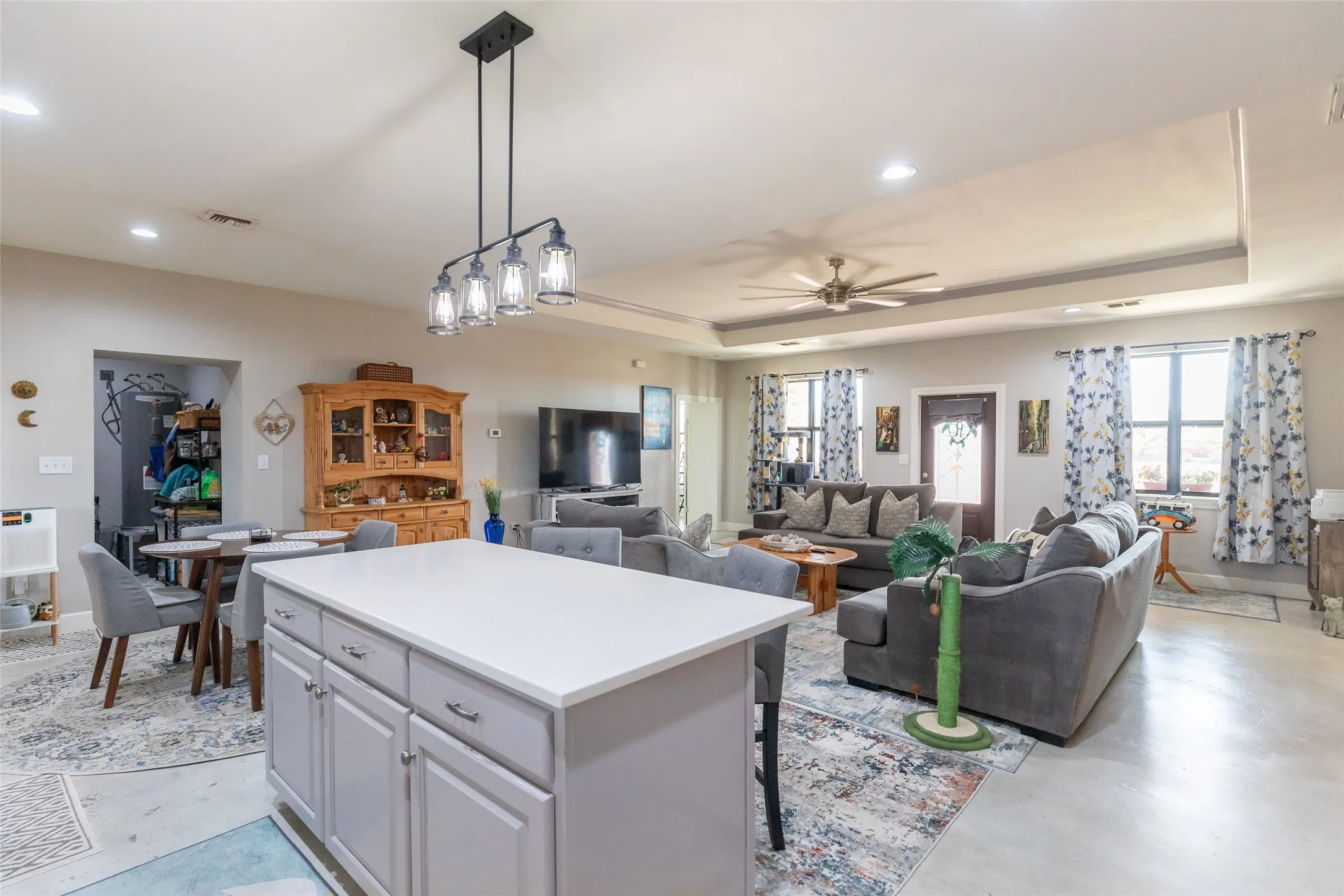 Kitchen island with stone countertop, suspended linear light fixture, recessed ceiling lights, tray ceiling with a ceiling fan, and multiple windows
