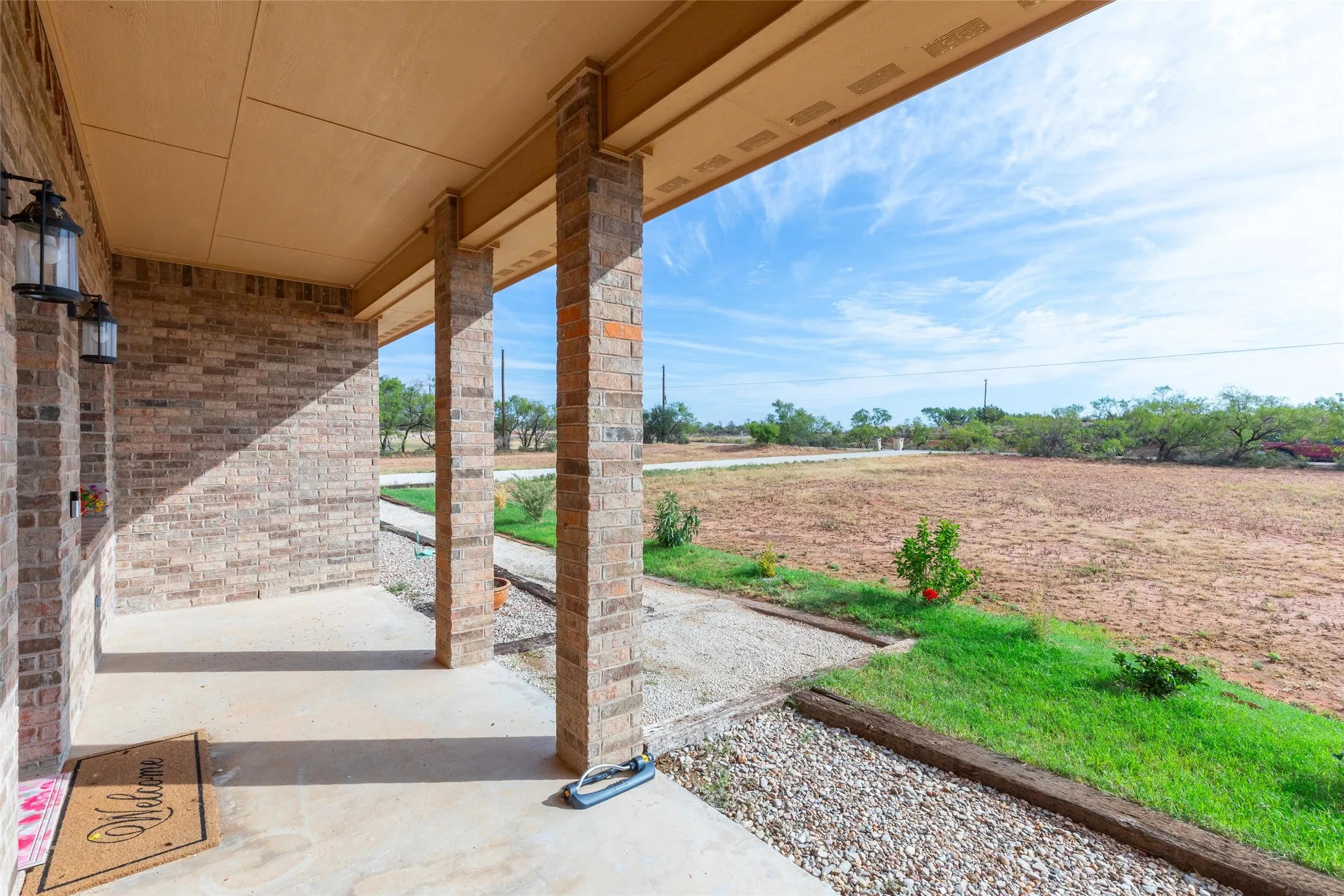Covered porch featuring brick columns and walls, concrete flooring, and exterior wall lanterns