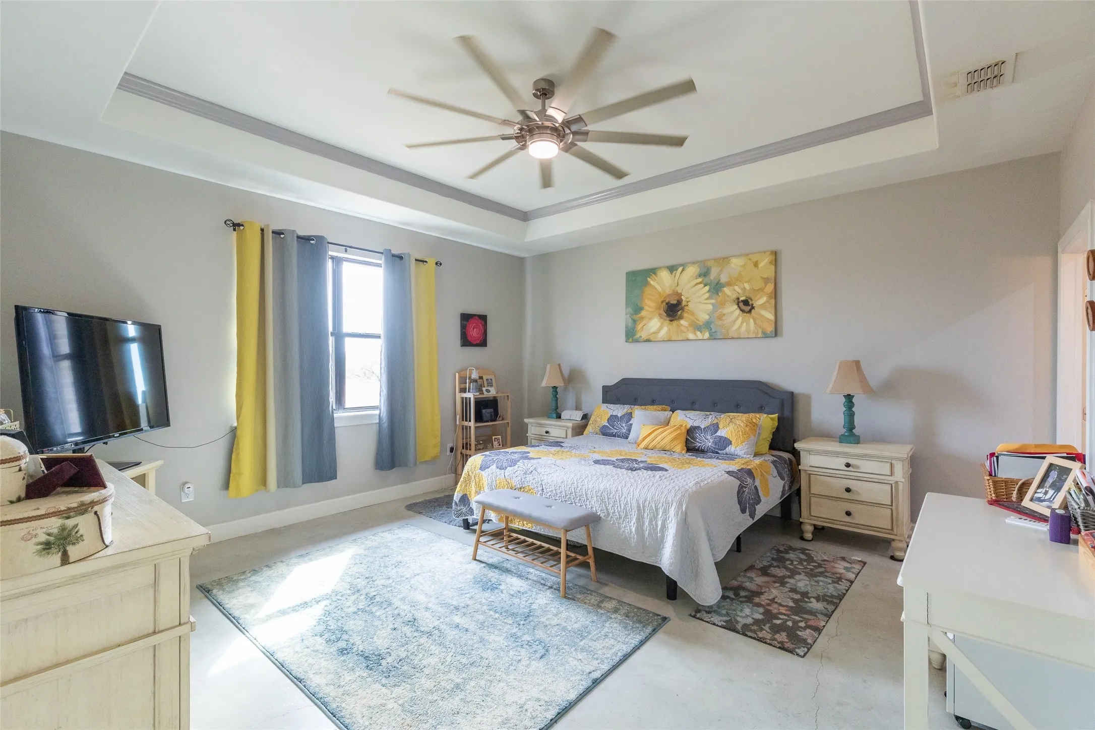 Tray ceiling with crown molding, ceiling fan with integrated lighting, window with ample natural light, light-toned walls, and durable flooring