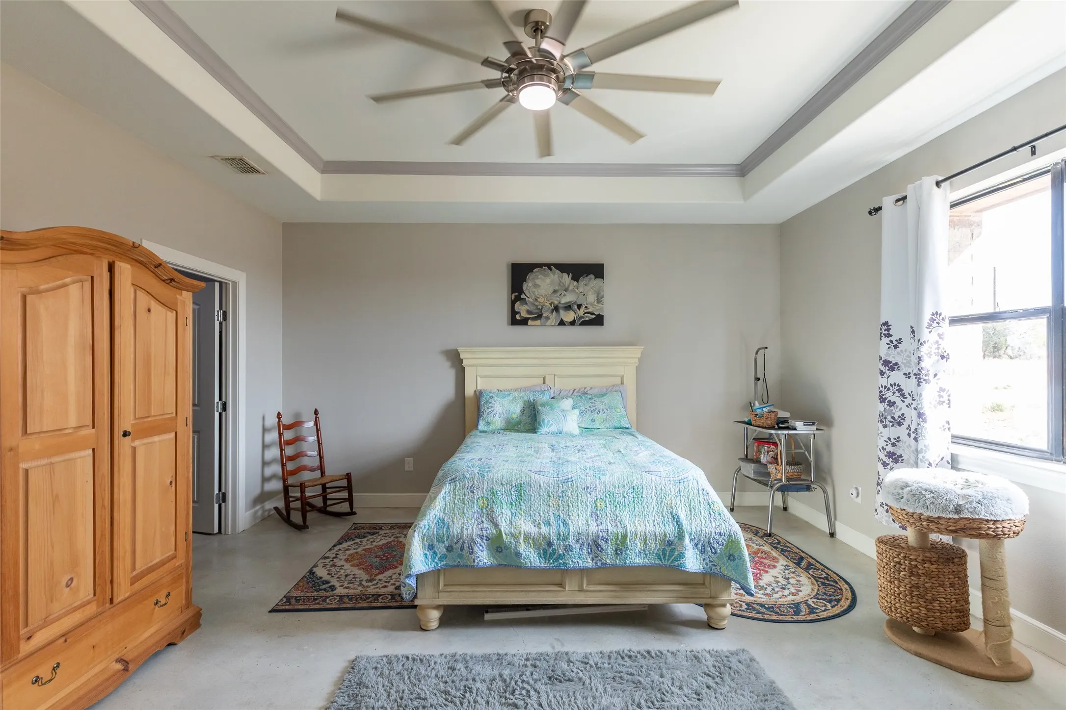 Tray ceiling with crown molding, large ceiling fan with integrated lighting, hard surface flooring, and a window with a dark frame