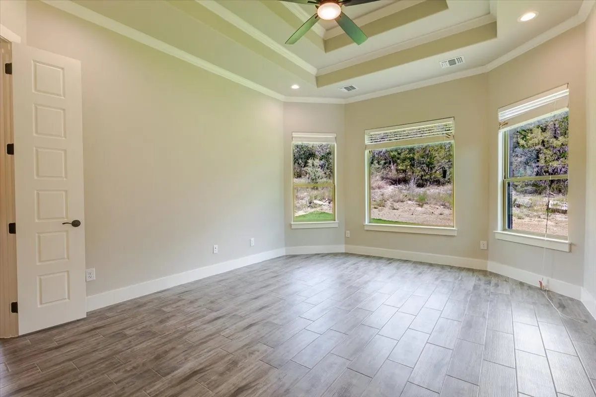 Tray ceiling with recessed lighting and a ceiling fan, three large windows, and gray wood-finish tile flooring