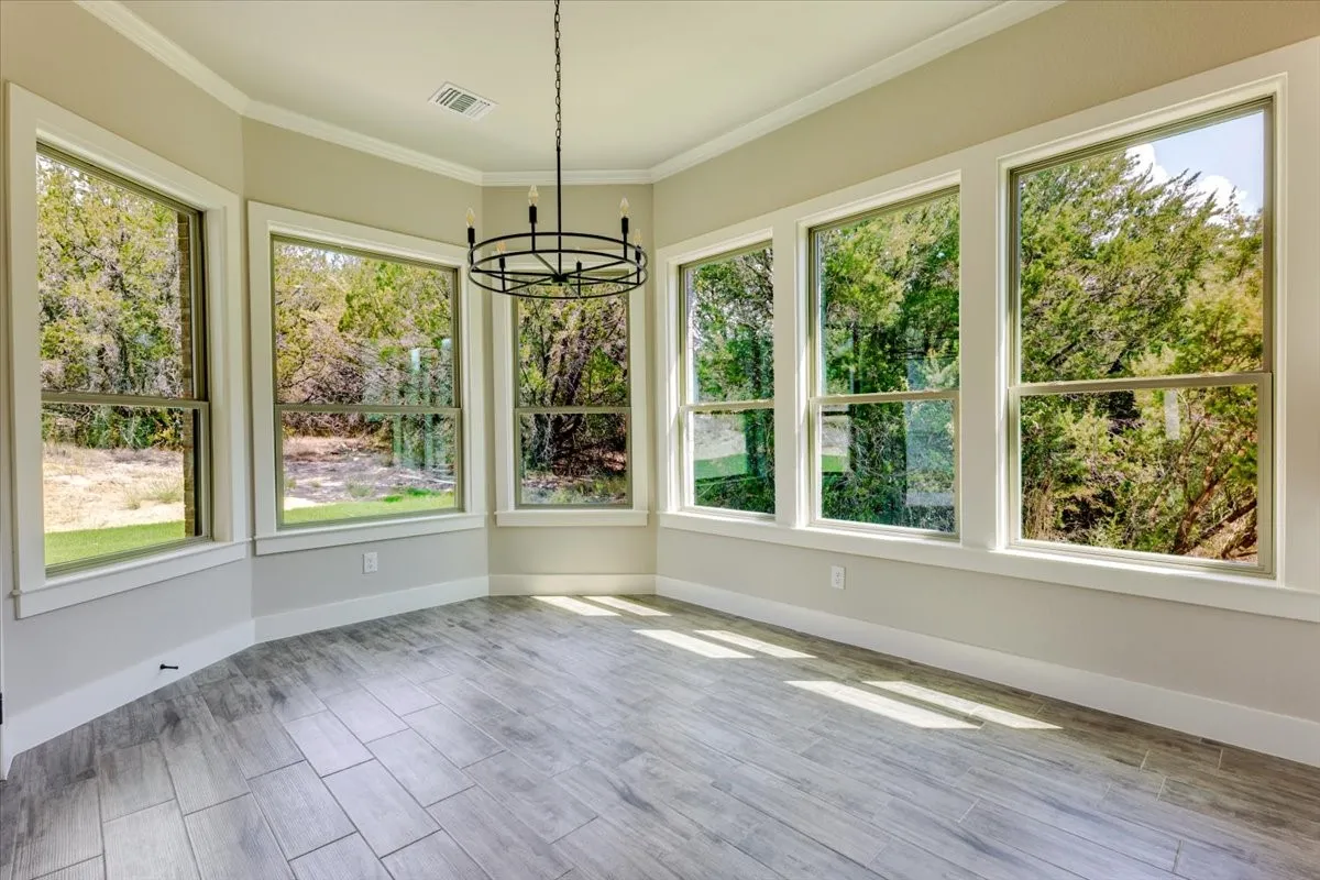 Bay window configuration, wood-finish flooring, crown molding, and a chandelier fixture