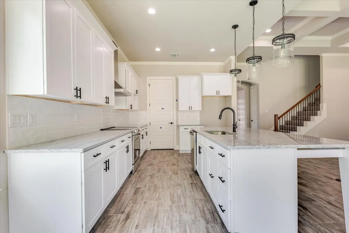 White shaker-style cabinetry with matte black hardware, light-toned countertops, wood-look flooring, and a kitchen island with integrated seating