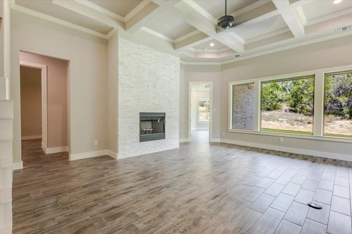 Coffered ceiling with a ceiling fan, tiled fireplace with a dark firebox, three large windows, and wood-finish flooring
