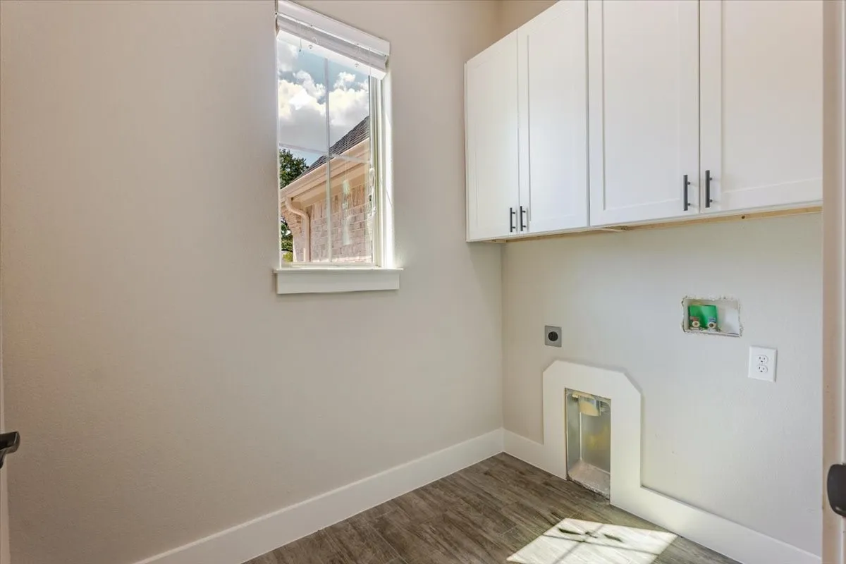 White shaker-style cabinetry with matte black hardware, wood-finish flooring, and a single window with roller shade