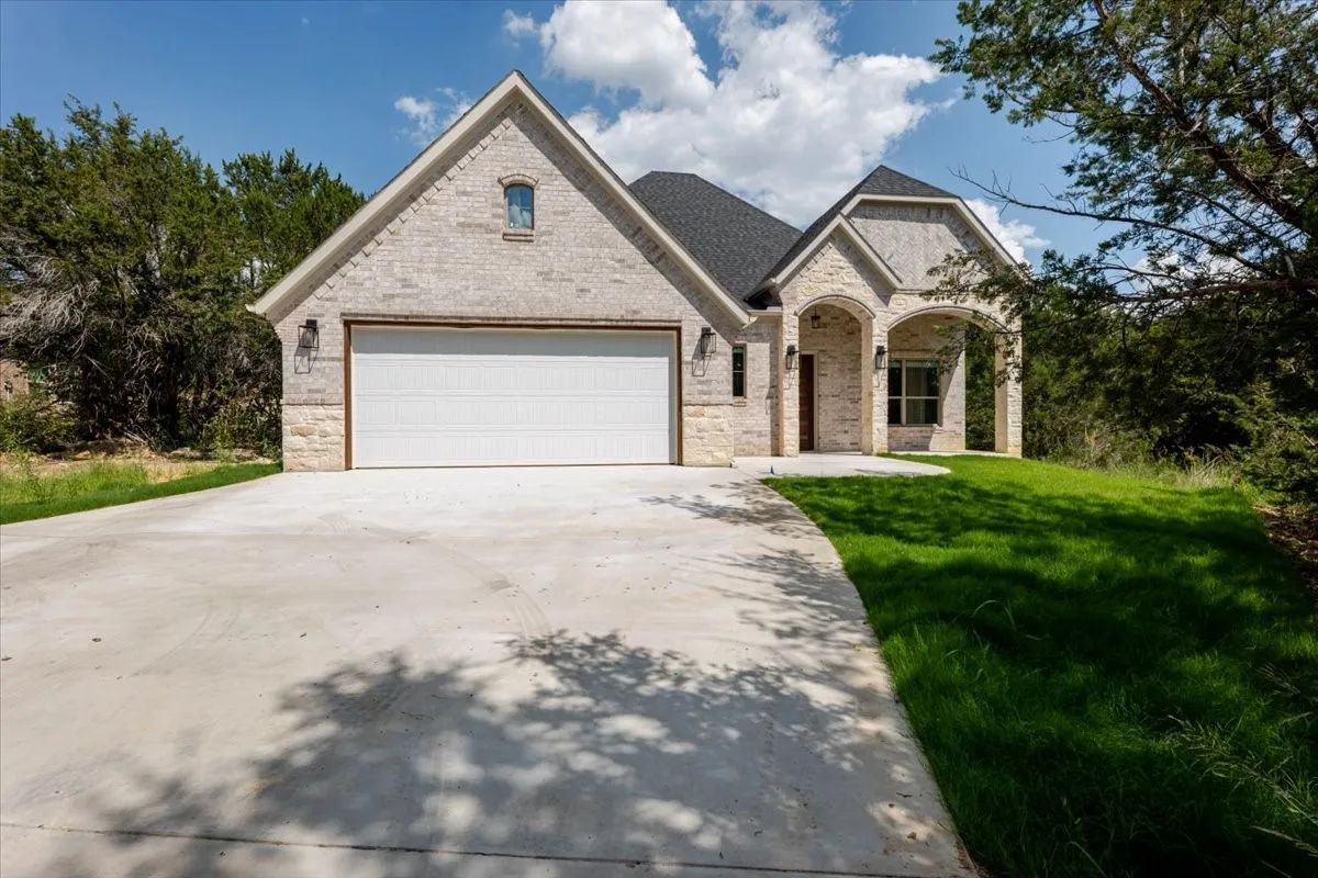 Stone and brick exterior with a dark shingle roof, arched entryways, and an attached two-car garage