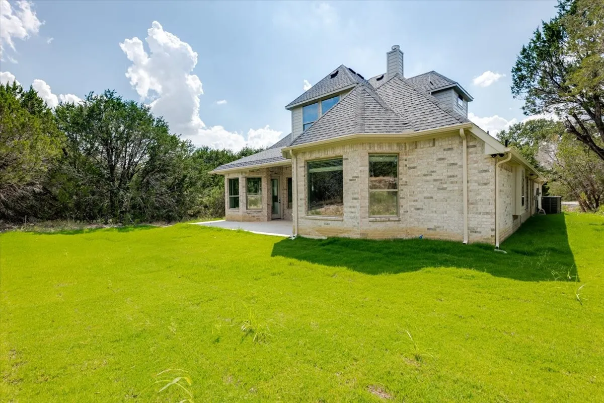 Spacious backyard featuring a manicured lawn, an expansive concrete patio, and mature perimeter trees