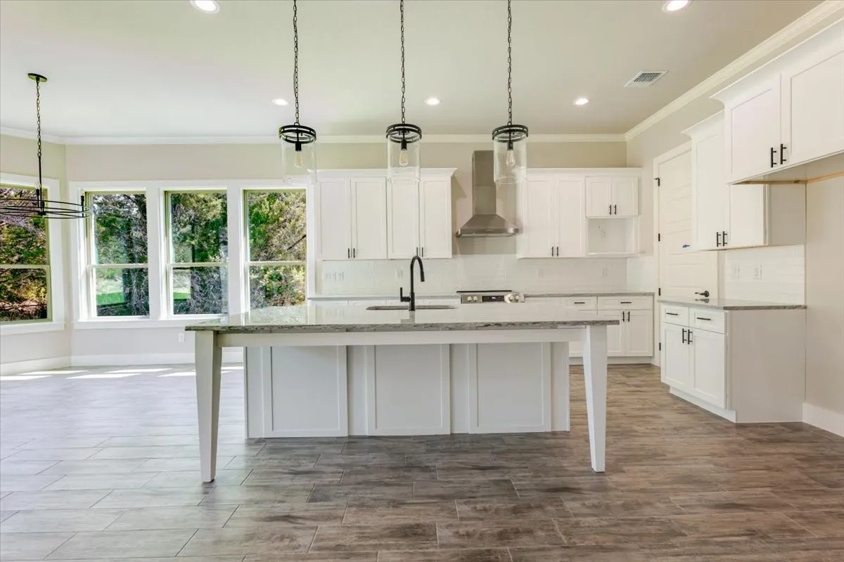 Kitchen featuring white shaker cabinetry, an expansive island with a light-toned countertop, a stainless steel range hood, white subway tile backsplash, and wood-finish flooring