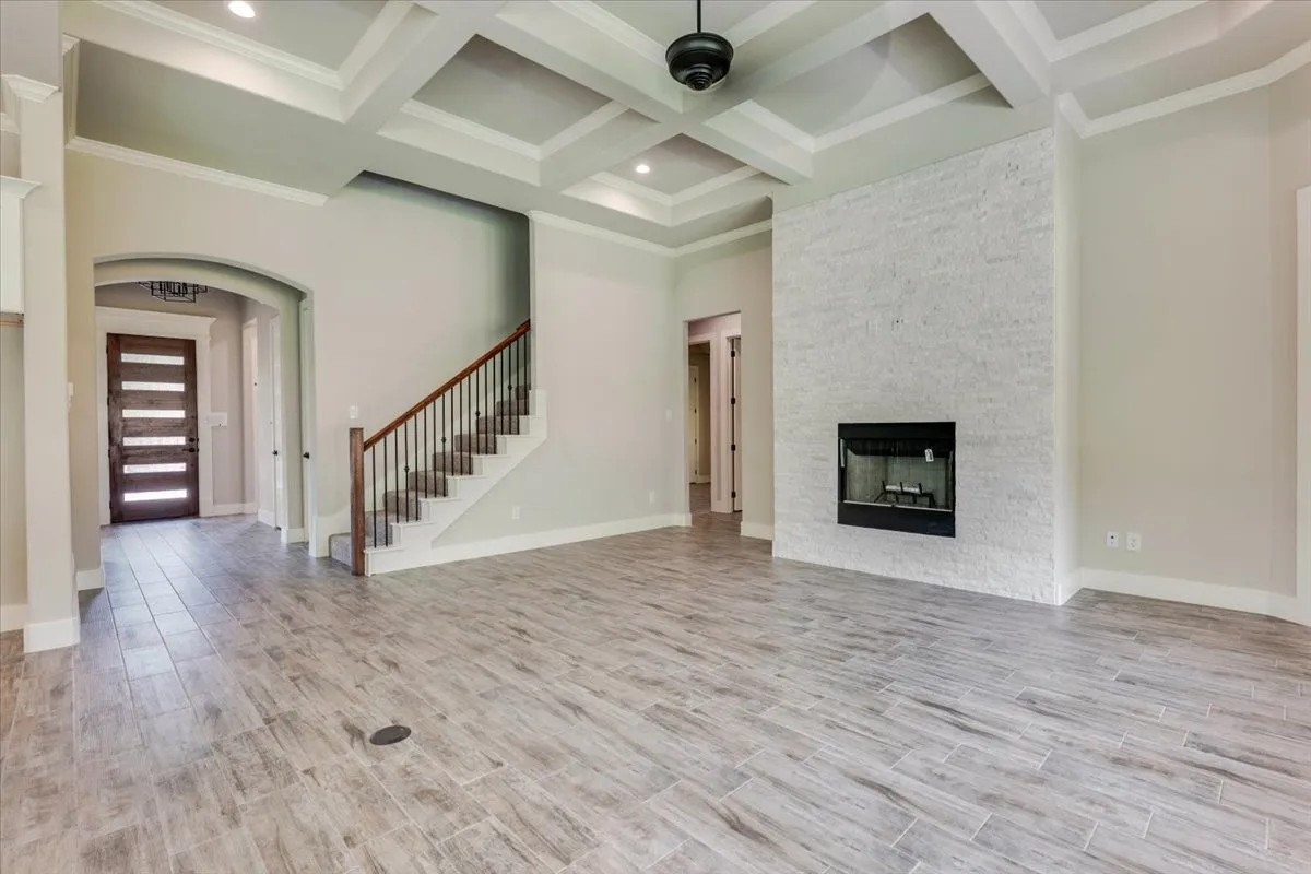 Coffered ceiling with recessed lighting, wood-finish flooring, a stone-clad fireplace with a dark metal insert, and a staircase with a wood handrail and dark metal balusters