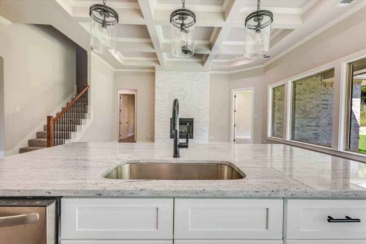 Kitchen island featuring a stainless steel sink with a matte black faucet, white shaker cabinetry, and a light-toned countertop