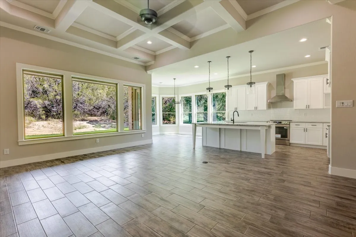 Coffered ceiling with recessed lighting, wood-finish flooring, white cabinetry, a kitchen island with a sink, and stainless steel appliances
