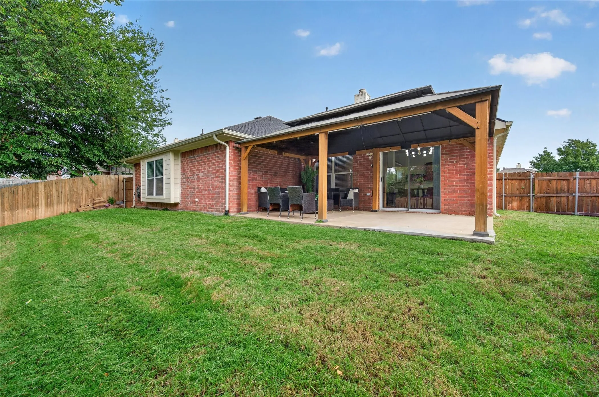 Rear exterior featuring red brick masonry, a covered patio with a wooden pergola, sliding glass doors, and wooden privacy fencing