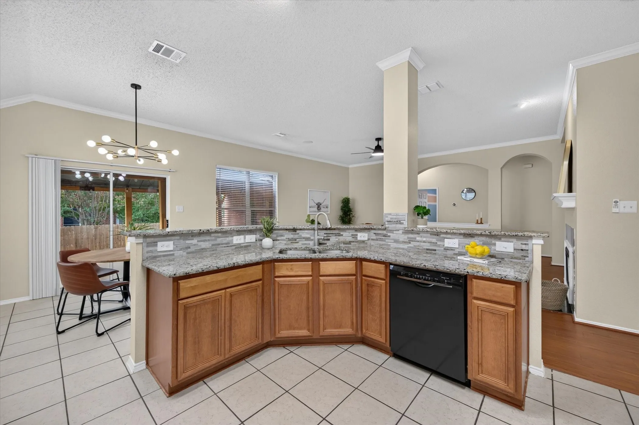 Kitchen featuring stone countertops, stone-tiled backsplash, built-in black dishwasher, wood cabinetry, and tile flooring
