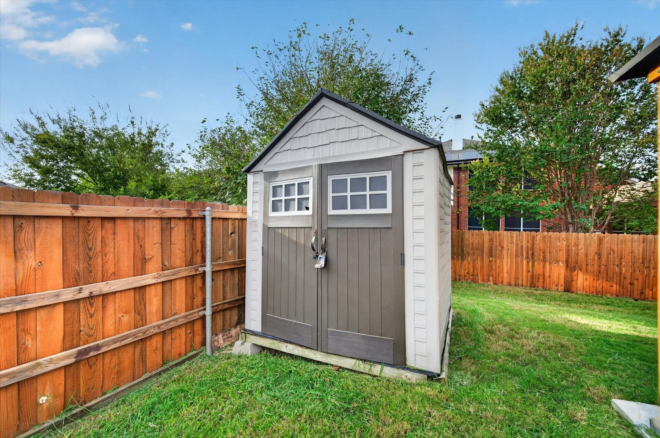 Detached storage shed featuring a dual-door entry, multi-pane windows, and shingle-style roof detailing, positioned within a fenced yard
