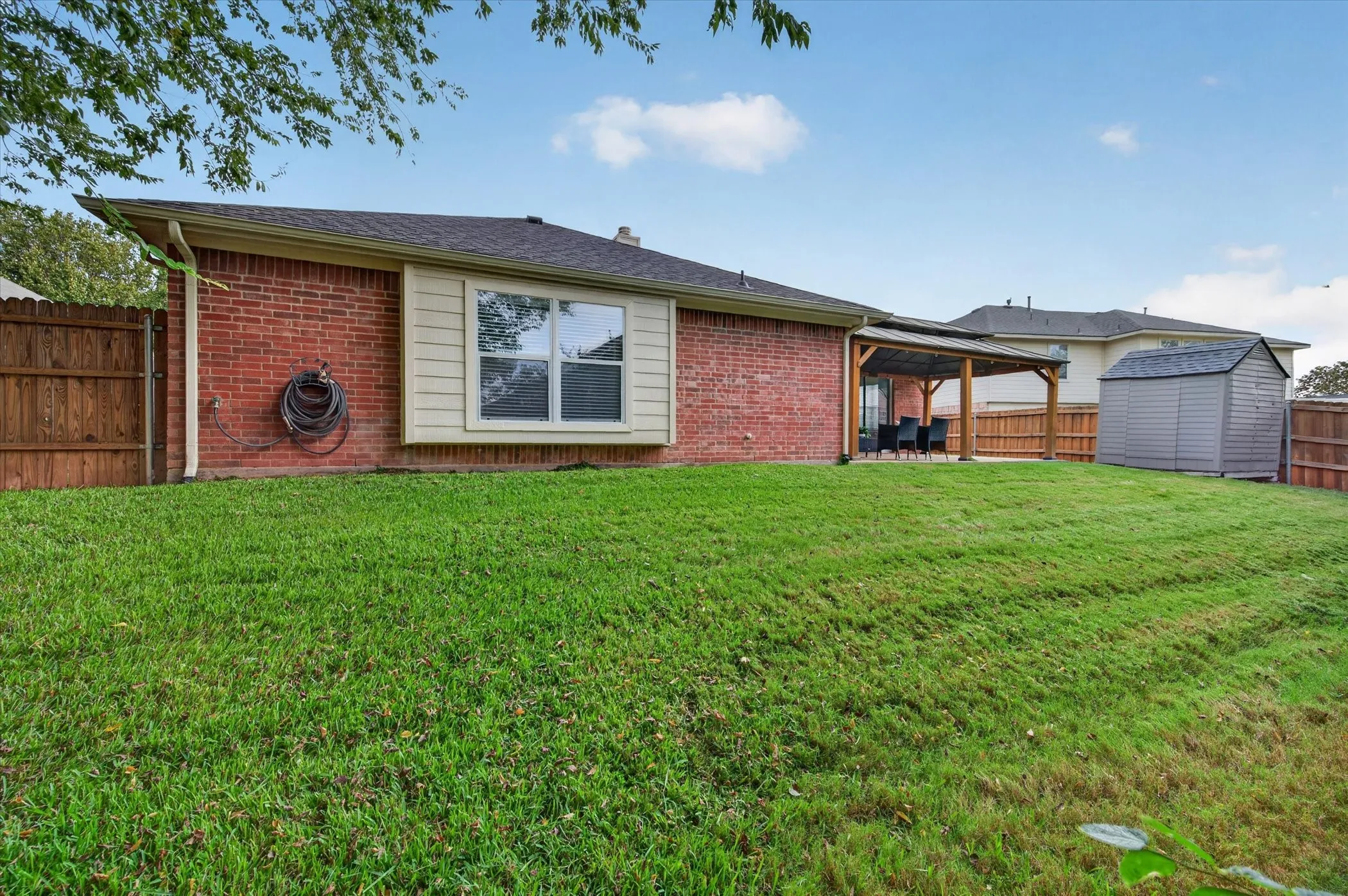 Brick exterior featuring a wooden pergola, expansive lawn, and fenced perimeter