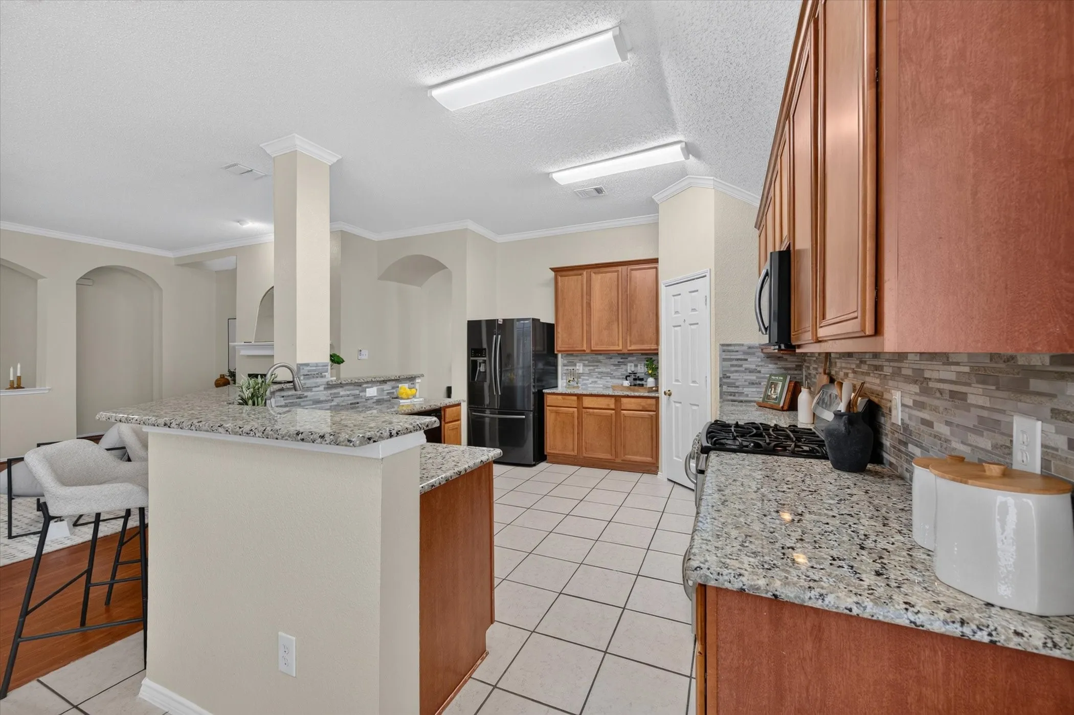 Kitchen featuring stone countertops, natural wood-finish cabinetry, tile flooring, built-in gas cooktop, and a tiered breakfast bar