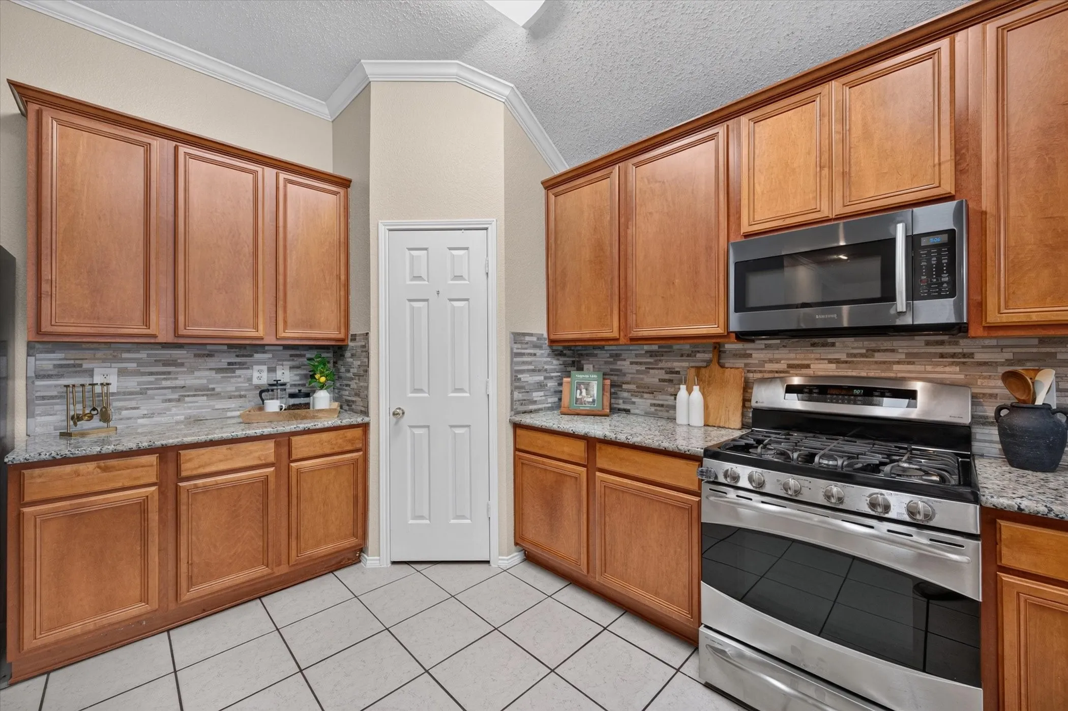 Kitchen featuring medium-tone wood cabinetry, stone-surface countertops, mosaic tile backsplash, stainless steel gas range, and built-in stainless steel microwave