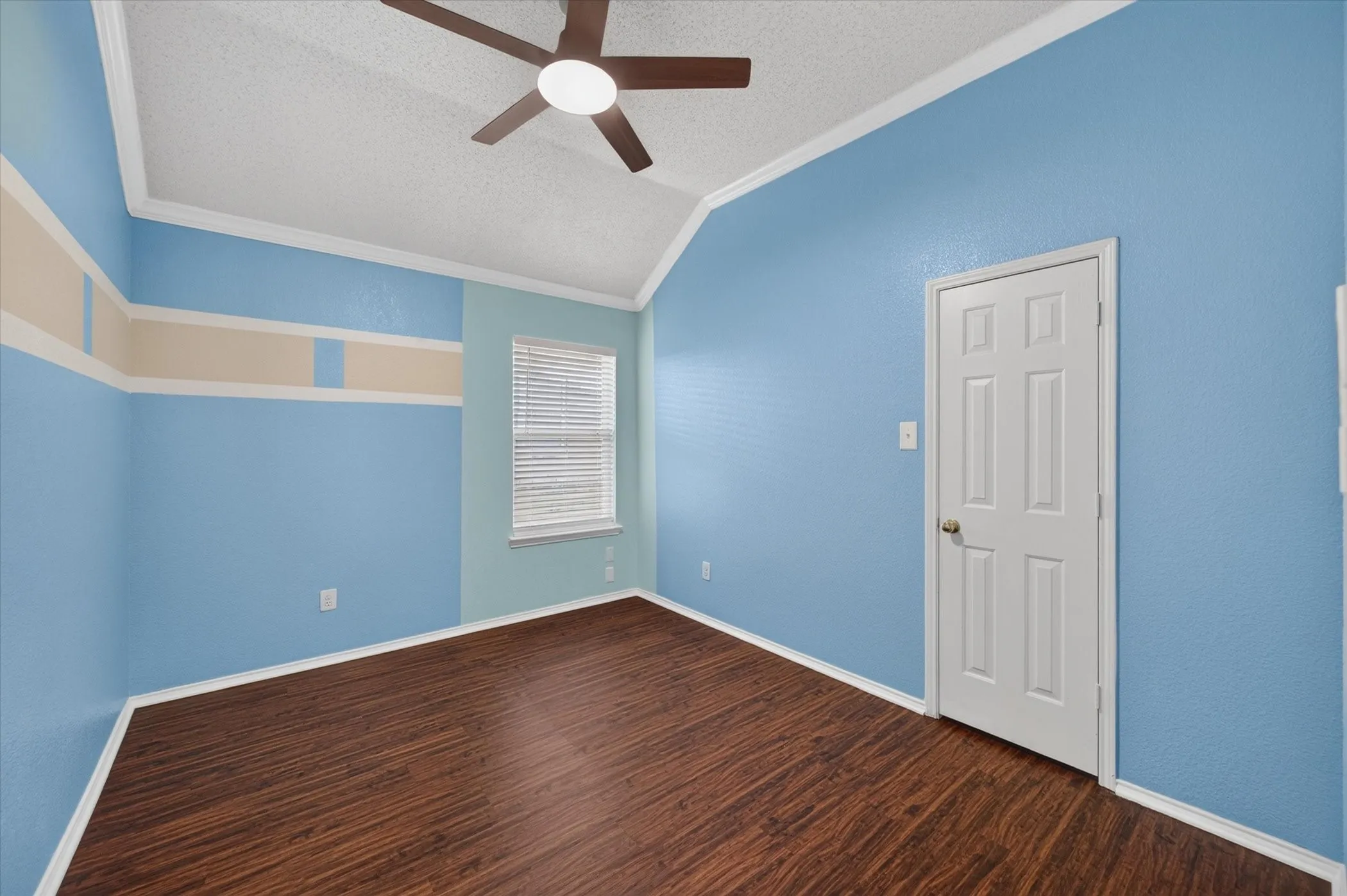Vaulted ceiling room featuring wood-finish flooring, a ceiling fan with integrated lighting, and a six-panel door
