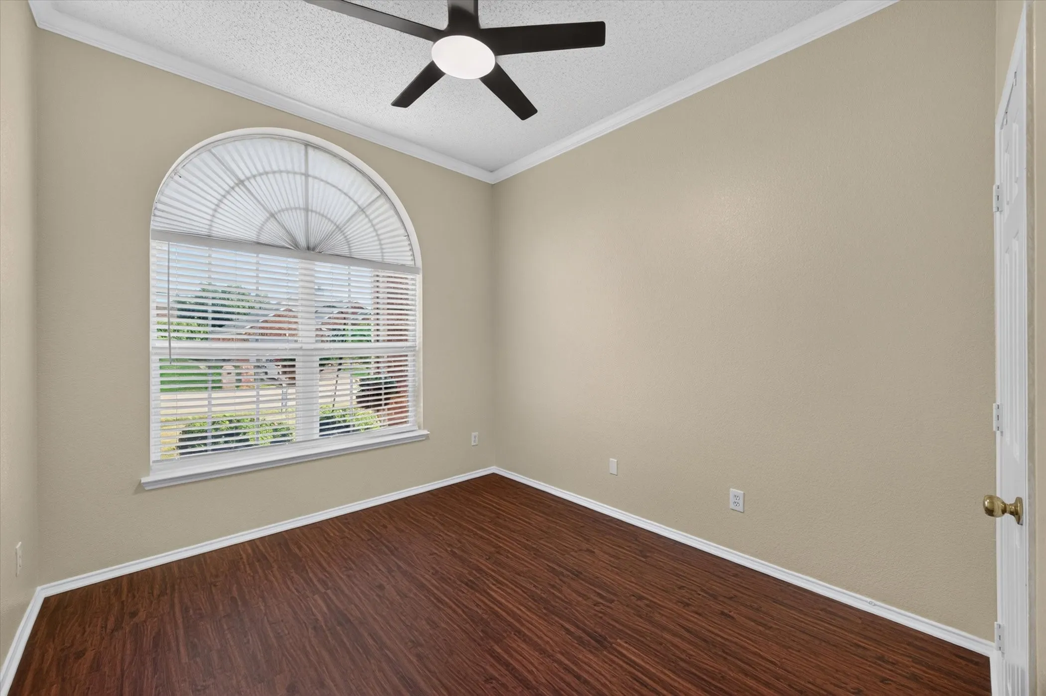 Room featuring wood-finish flooring, a large arched window, and a ceiling fan with integrated lighting