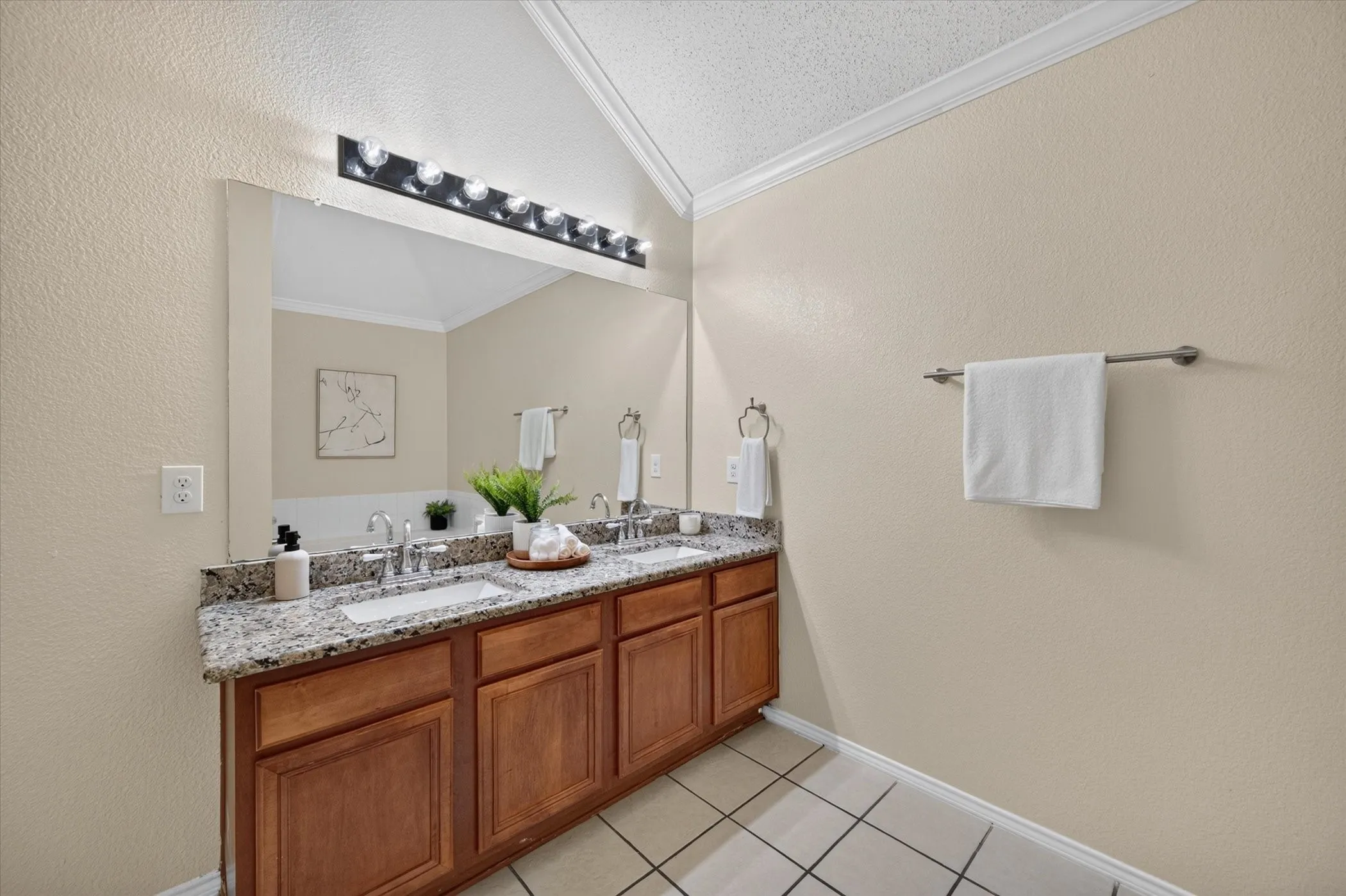 Double vanity featuring stone-finish countertops, dual integrated sinks, wood-finish cabinetry, and a full-width mirror with an overhead multi-bulb light fixture