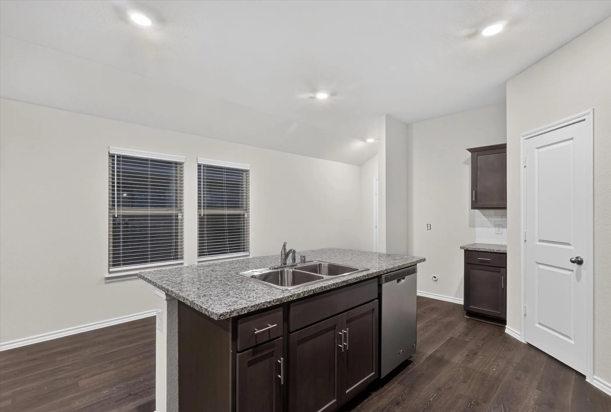 Kitchen island with a double basin sink, granite-style countertop, and dark wood cabinetry