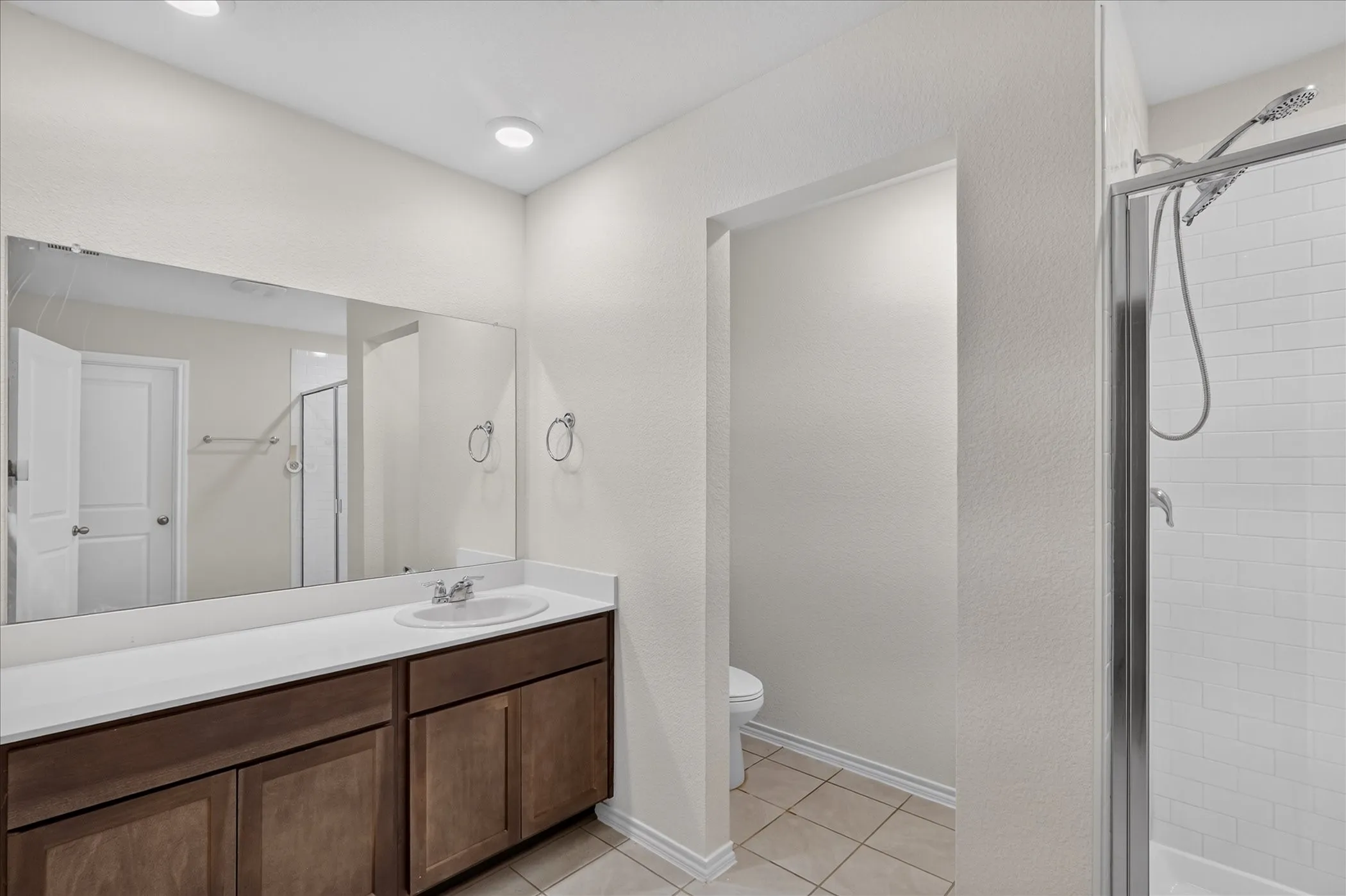 Dual vanity with wood-finish cabinetry, integrated sink, and expansive mirror