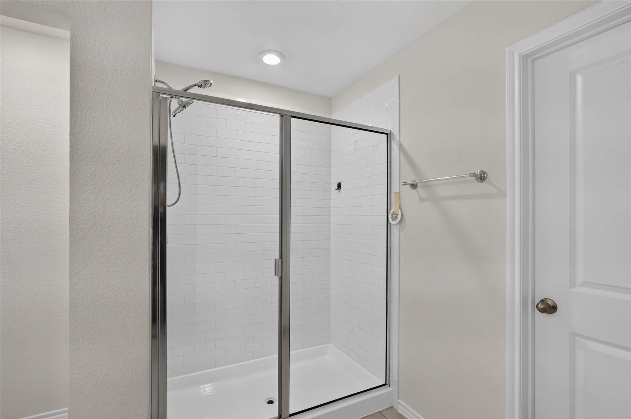 Shower enclosure with clear glass doors, subway tile surround, a chrome shower head, and recessed lighting