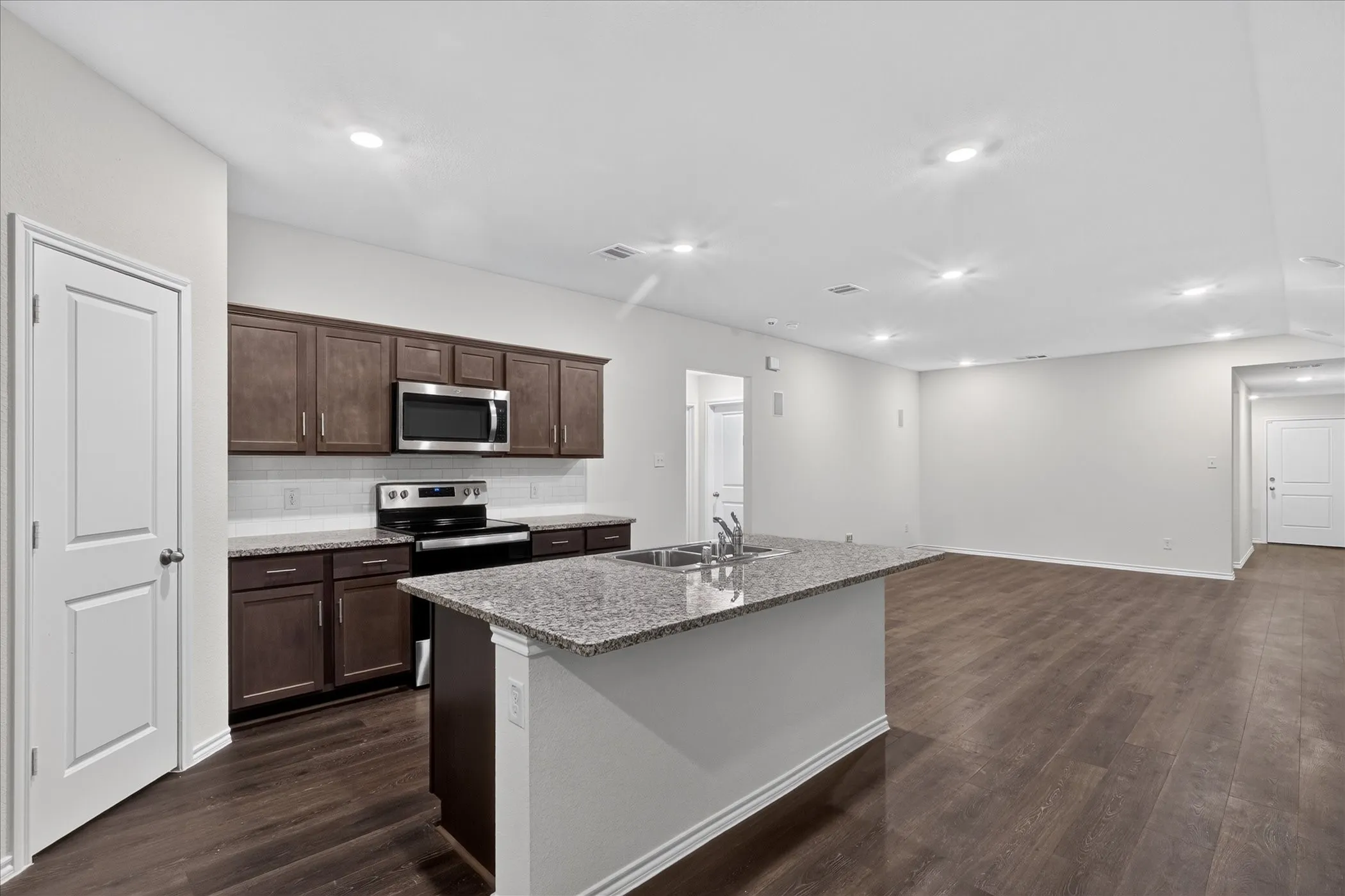 Kitchen featuring granite countertops, dark wood-finish cabinetry, stainless steel appliances, and a subway tile backsplash