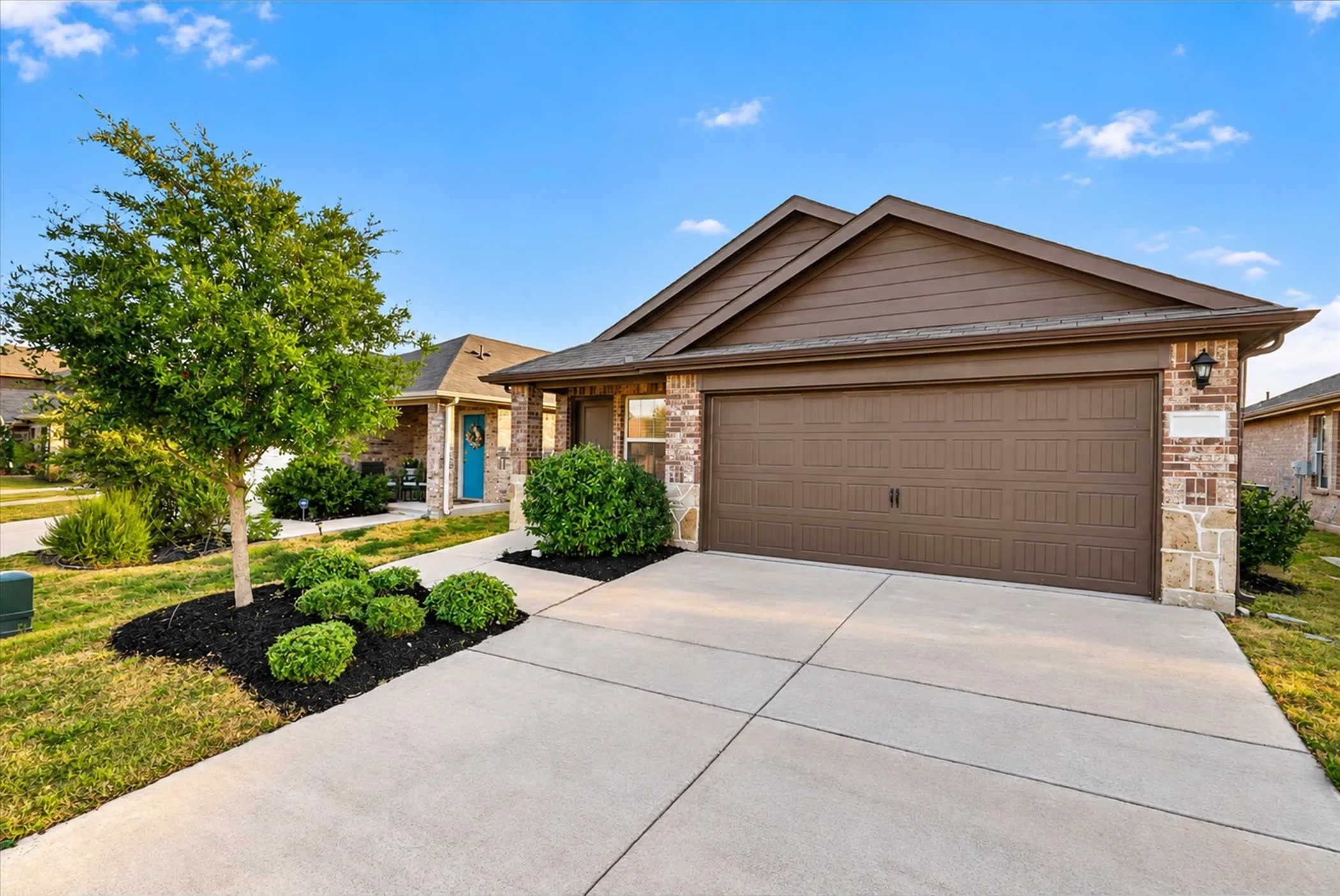 Brick and stone facade, attached garage, concrete driveway, landscaped front yard, and a covered entry