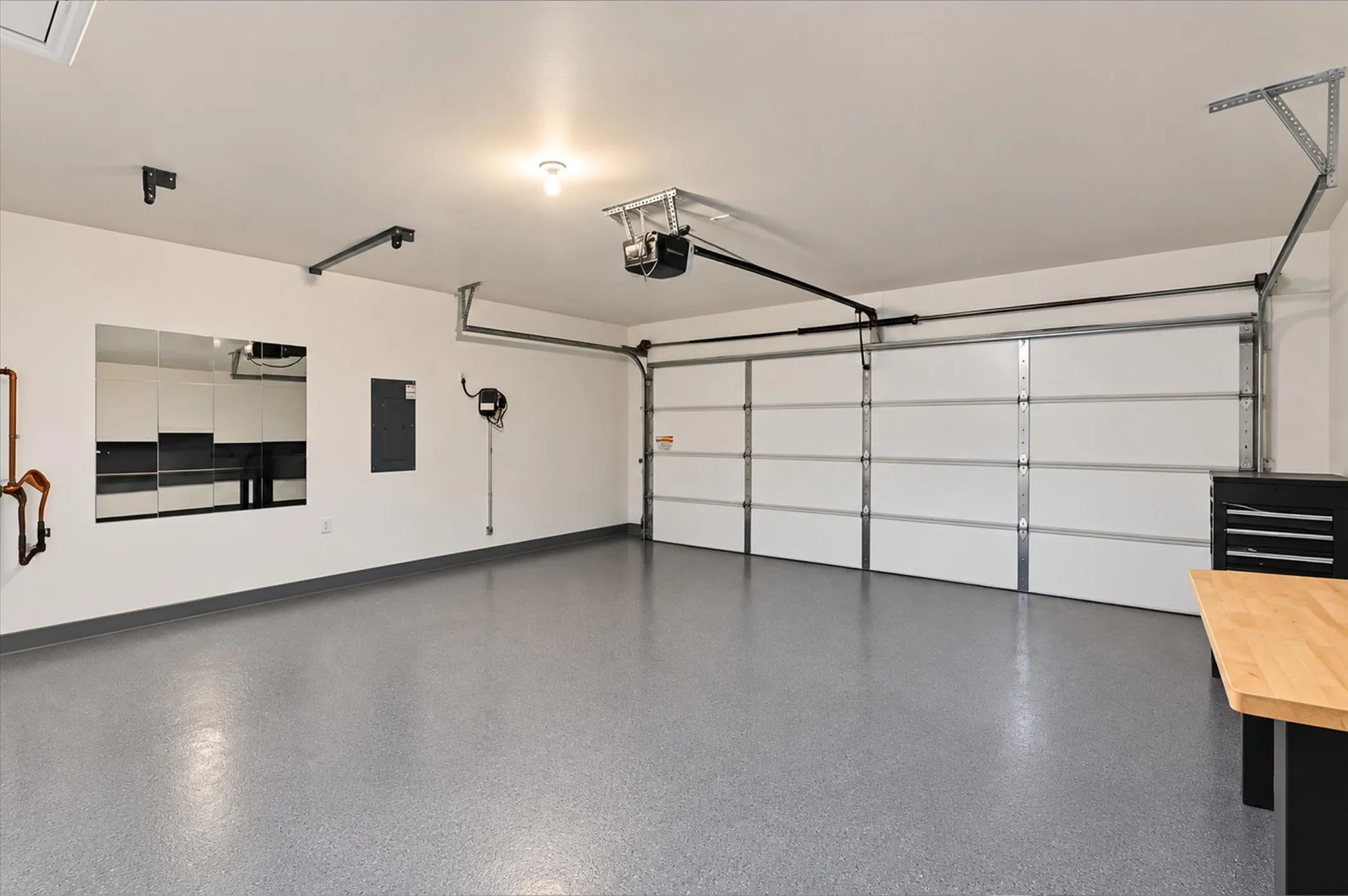 Spacious garage with light gray speckled flooring, white overhead sectional door, and overhead lighting