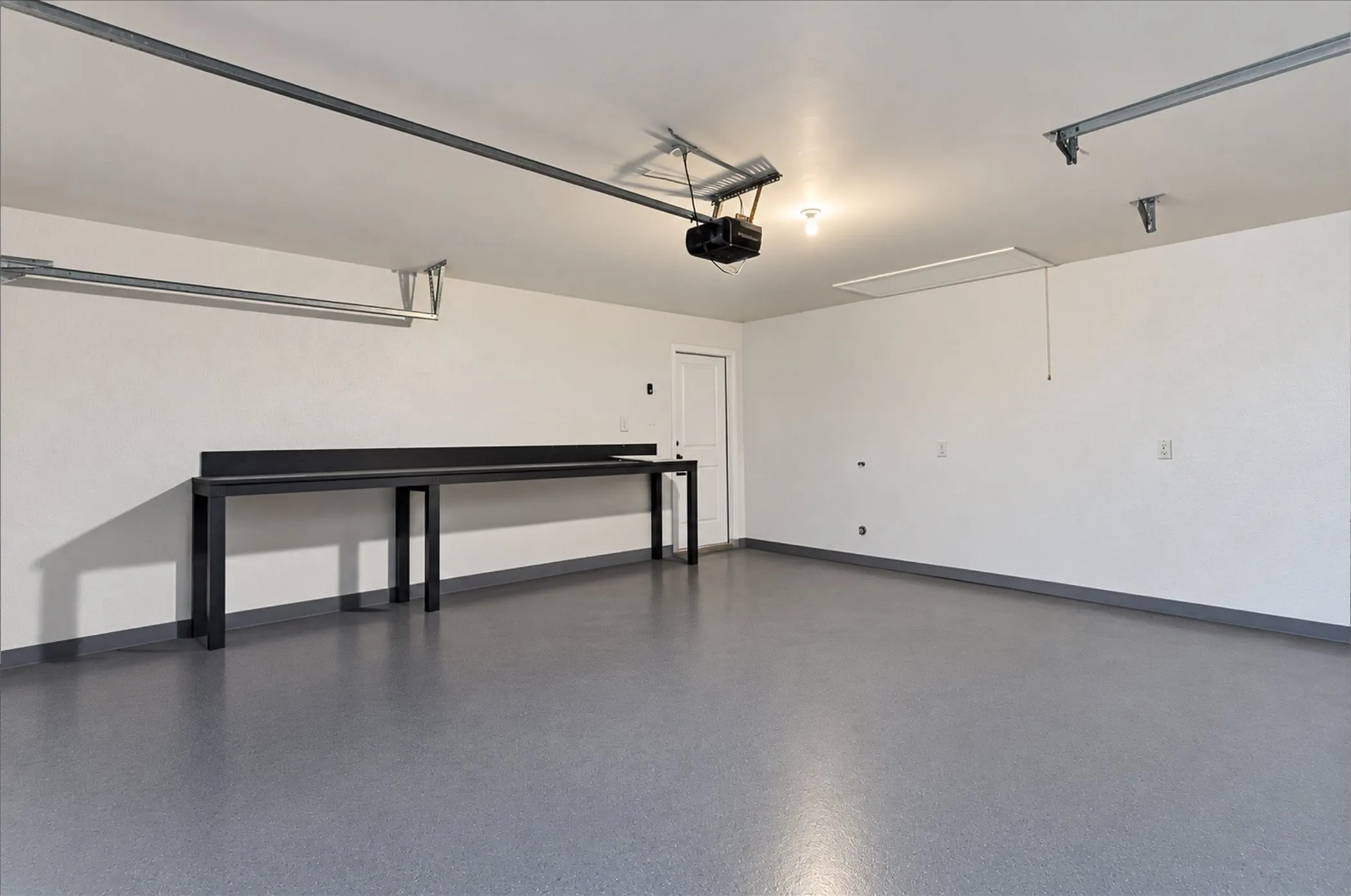 Expansive garage with durable epoxy flooring, an integrated workbench, and overhead lighting