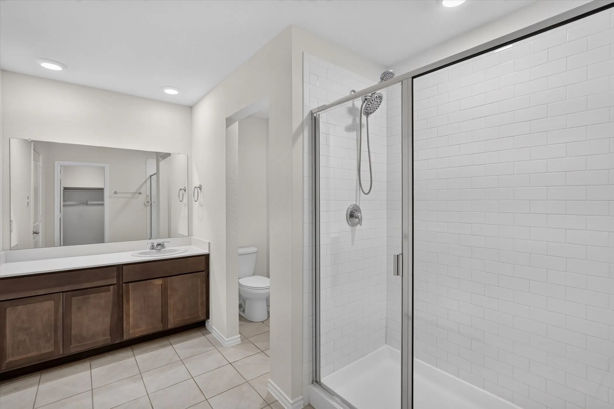 Dual sink vanity with dark wood-finish cabinetry, a large mirrored wall, and recessed lighting