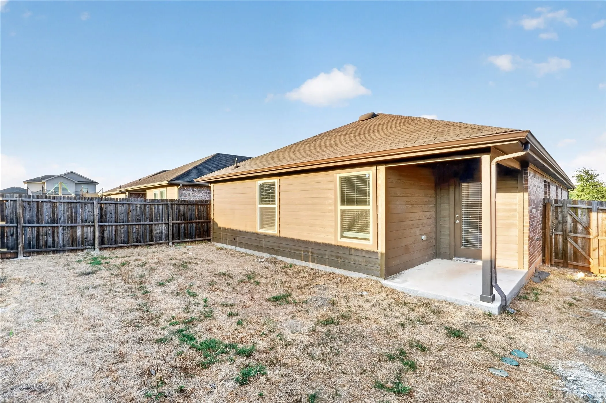 Rear exterior featuring a covered patio, wood-finish siding, brick accents, and a privacy fence