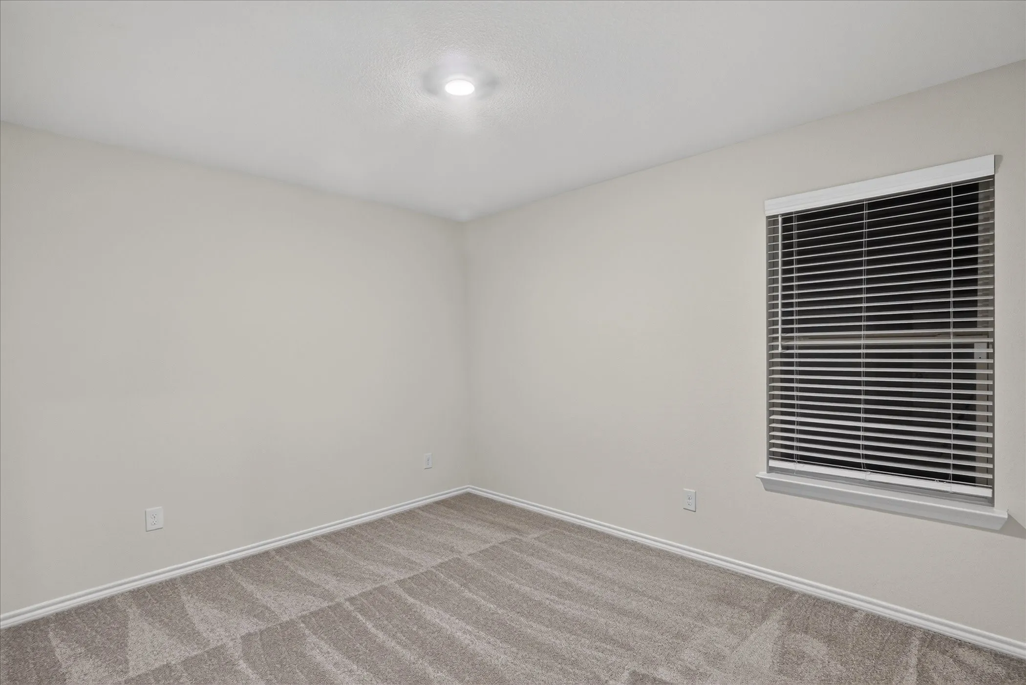 Neutral-toned walls with recessed lighting, carpeted flooring, and a single window with blinds